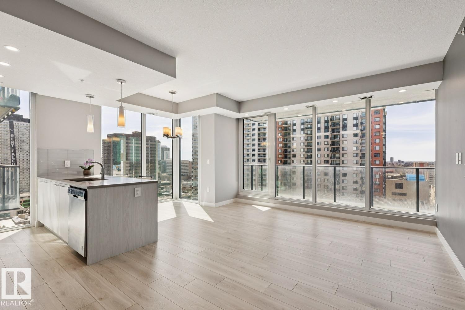 Open-concept living area with extensive floor-to-ceiling windows, light wood-finish flooring, a contemporary kitchen island with an integrated sink, and recessed ceiling lighting - #1601 10180 103 St Nw, Edmonton, AB - Indoor Photo Showing Kitchen With Upgraded Kitchen