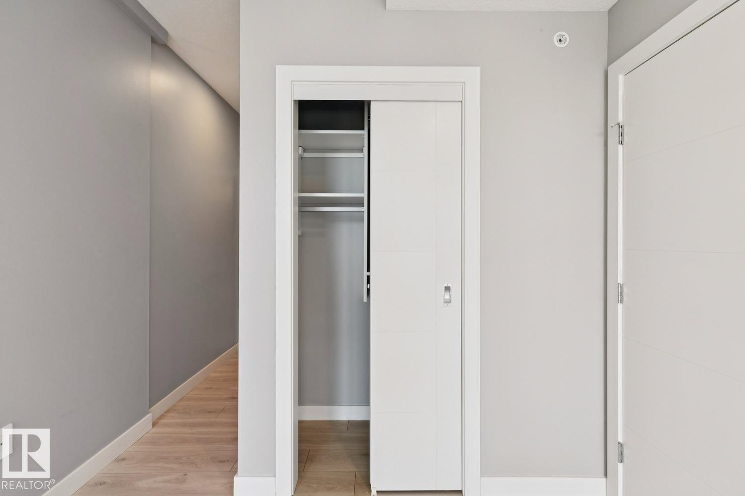 Recessed closet with a sliding panel door, integrated shelving, and hanging rods - #1601 10180 103 St Nw, Edmonton, AB - Indoor Photo Showing Other Room
