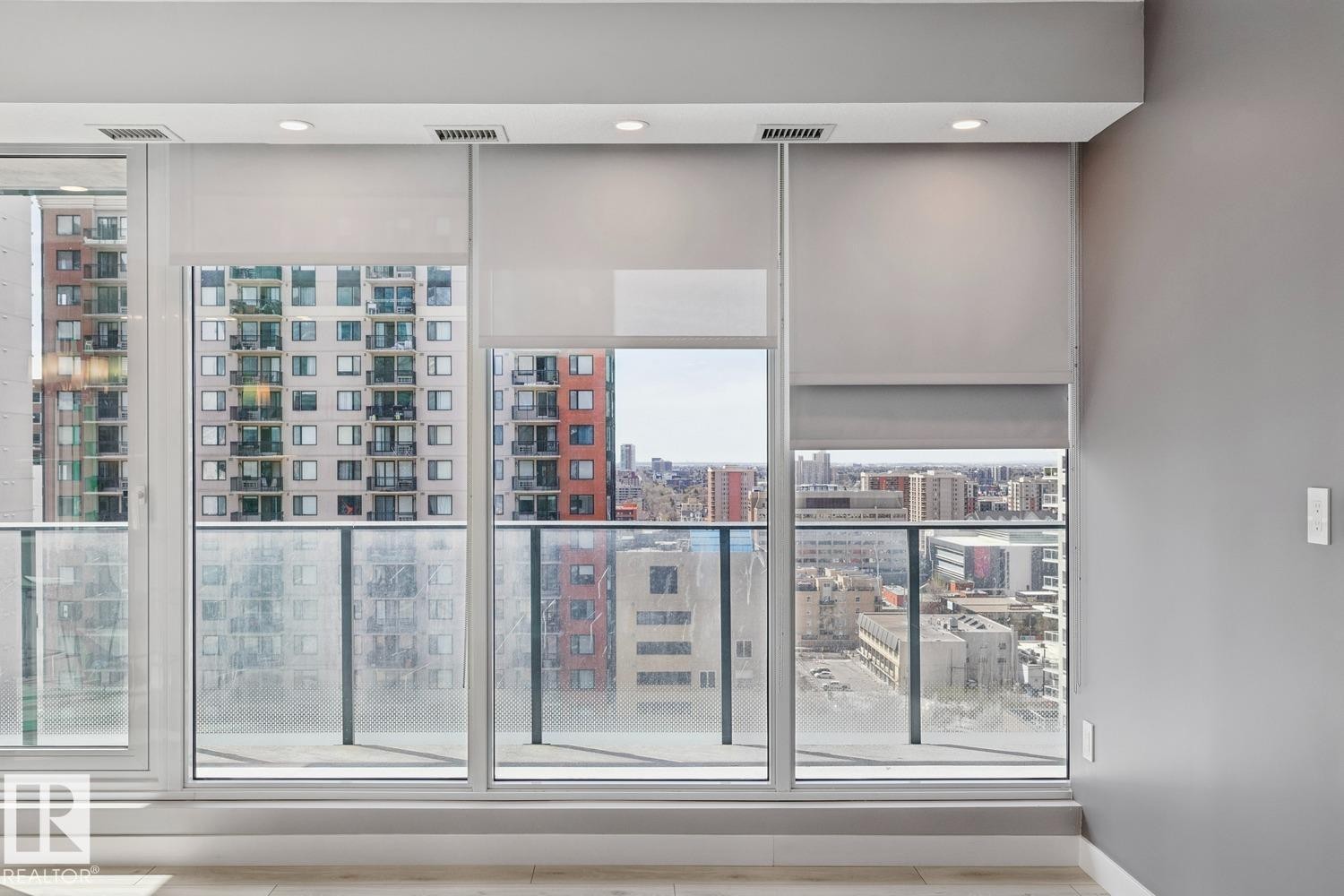 Floor-to-ceiling windows with roller shades, recessed lighting, light wood-finish flooring, and a glass-paneled balcony railing - #1601 10180 103 St Nw, Edmonton, AB - Indoor Photo Showing Other Room
