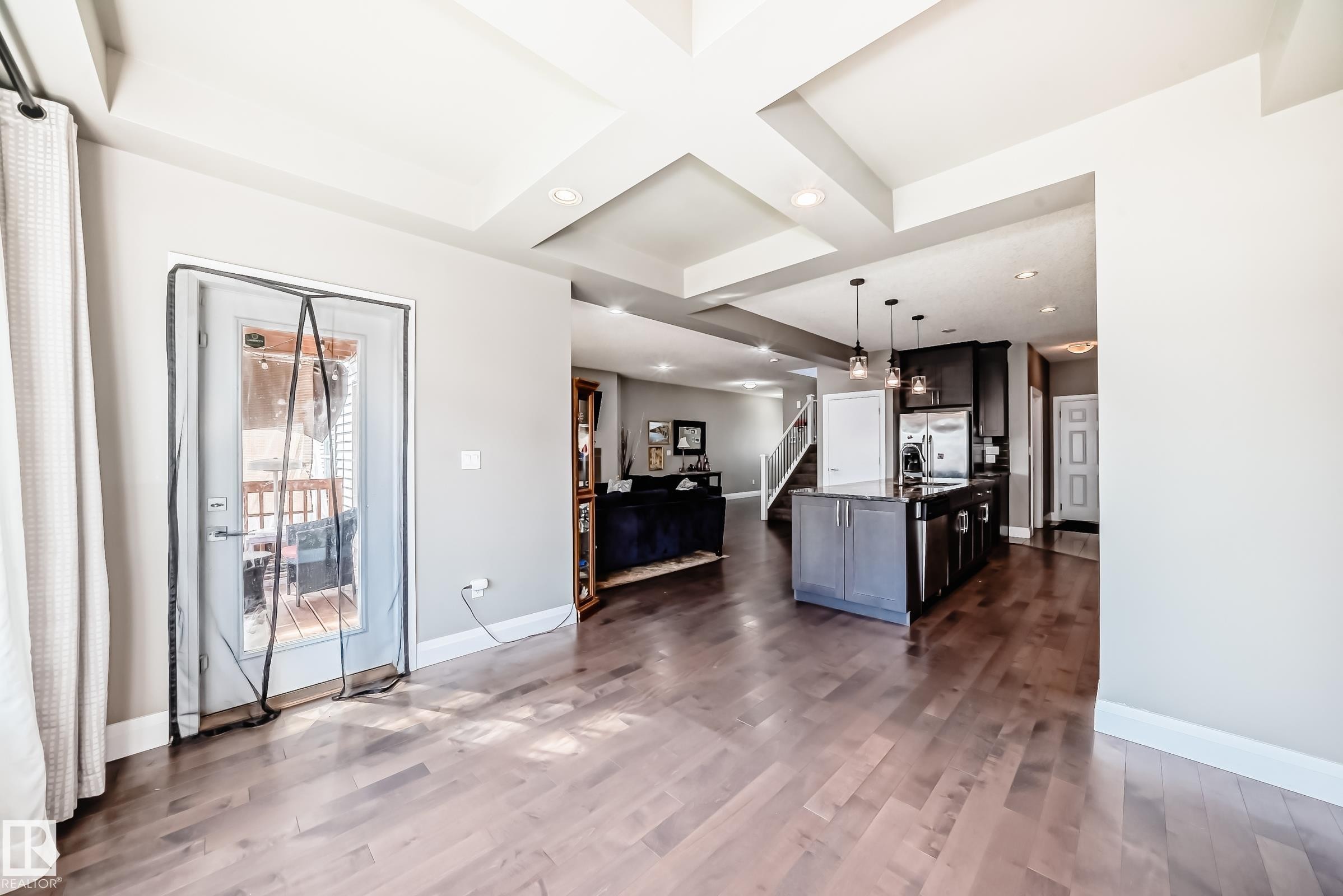 Spacious open-concept interior featuring wood-finish flooring, a kitchen island with pendant lighting, and a glass-paneled exterior door - 4155 Charles Link, Edmonton, AB - Indoor Photo Showing Other Room
