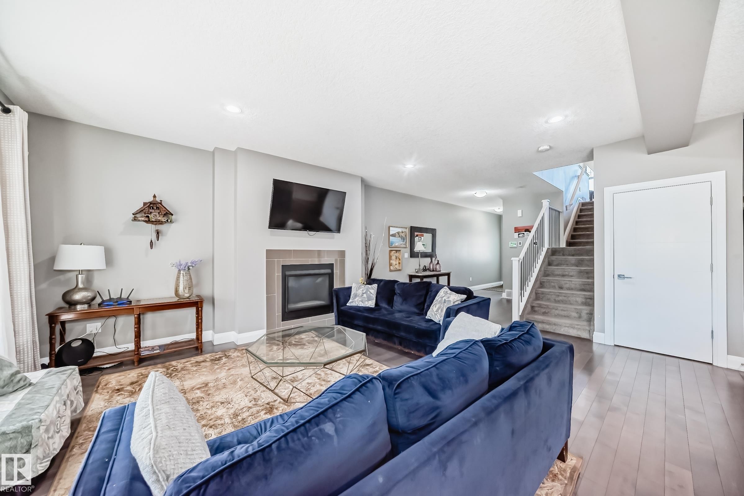 Spacious living area featuring a fireplace with tile surround, recessed lighting, wood-finish flooring, and a carpeted staircase with white railings - 4155 Charles Link, Edmonton, AB - Indoor Photo Showing Living Room With Fireplace