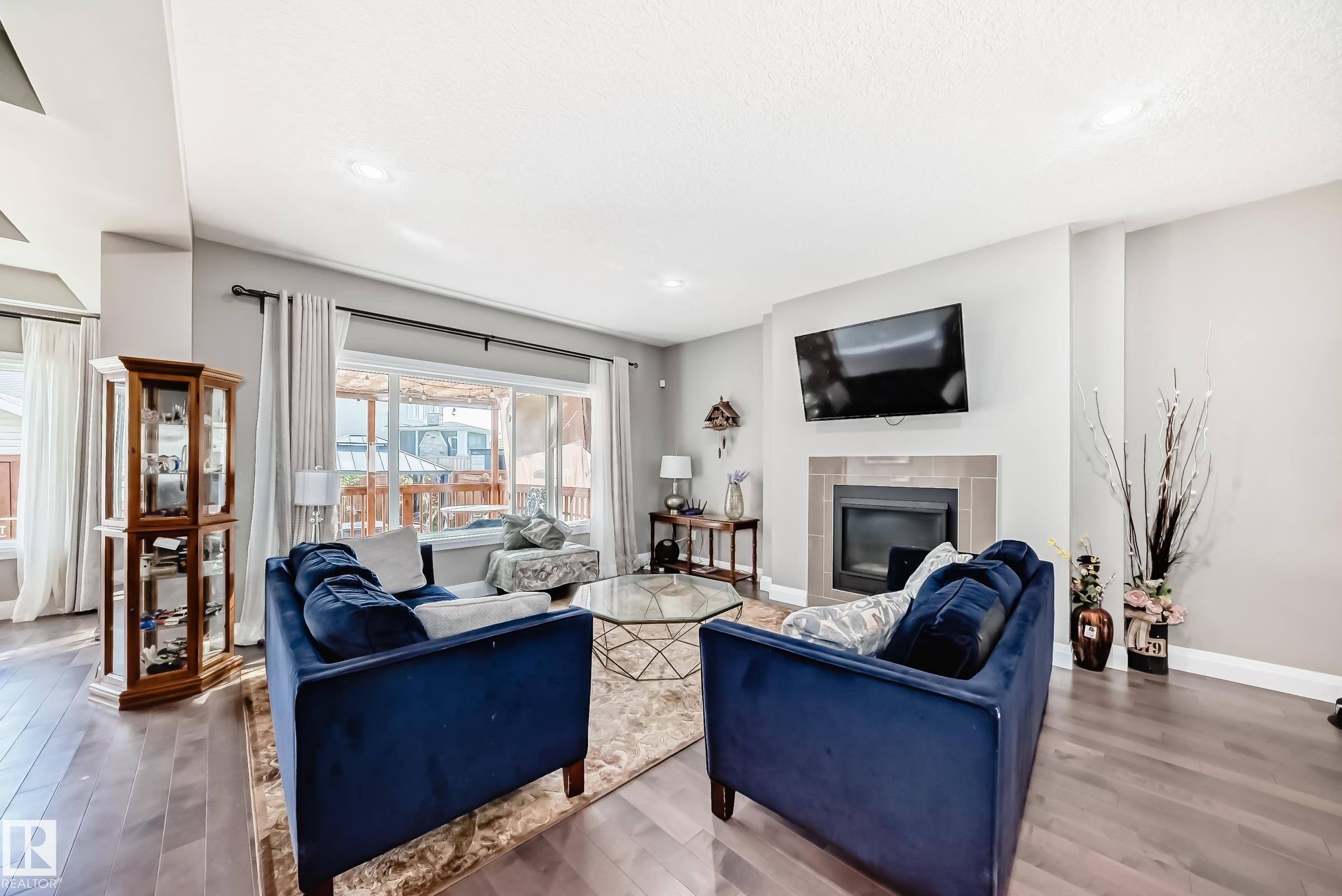 Living area featuring wood-finish flooring, a contemporary fireplace with a tile surround, recessed lighting, and large sliding glass doors leading to an exterior space - 4155 Charles Link, Edmonton, AB - Indoor Photo Showing Living Room With Fireplace