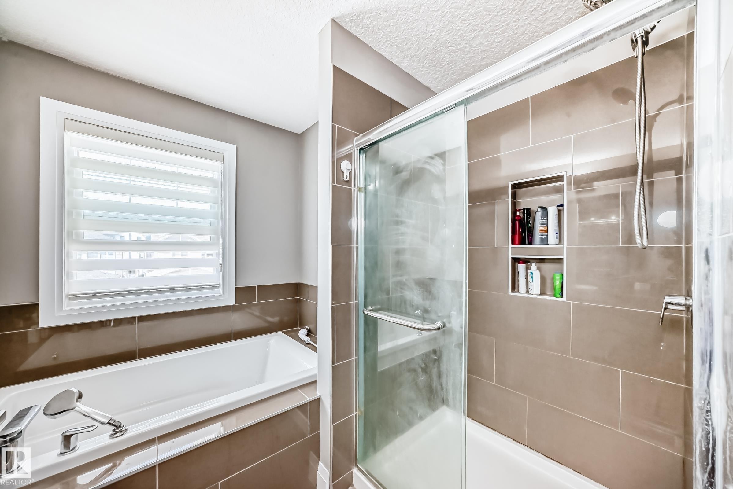 Contemporary bathroom featuring a built-in tub with chrome fixtures, a separate glass-enclosed shower, neutral-toned wall tiles, and a window with horizontal blinds - 4155 Charles Link, Edmonton, AB - Indoor Photo Showing Bathroom