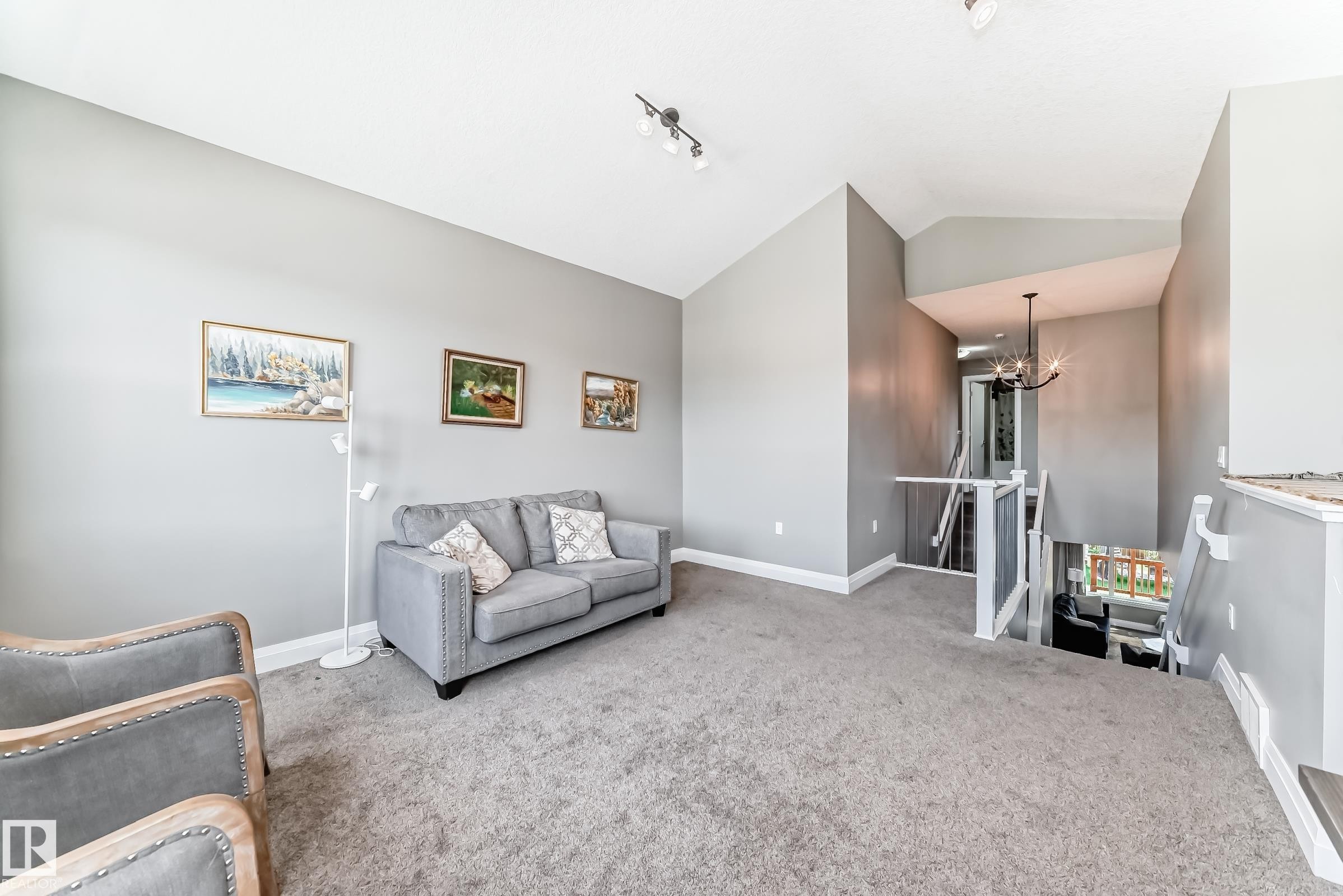 Carpeted upper level featuring vaulted ceilings, track lighting, and a prominent staircase with white railings - 4155 Charles Link, Edmonton, AB - Indoor