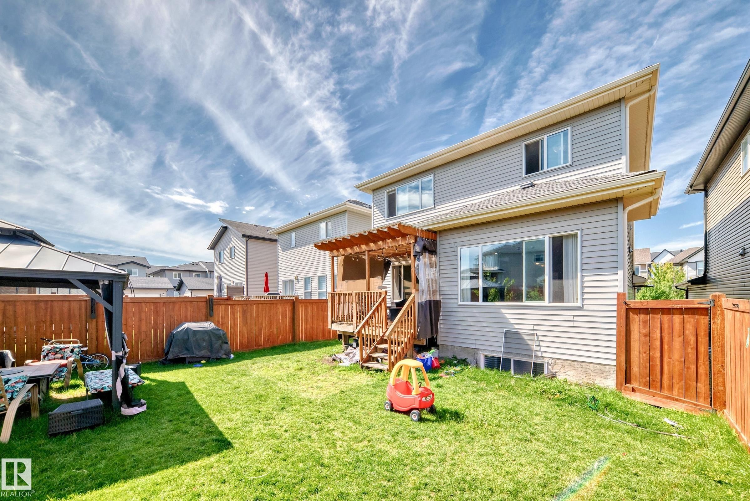 Expansive fenced backyard featuring a wood deck with a pergola, a level lawn area, and a lower-level window - 4155 Charles Link, Edmonton, AB - Outdoor
