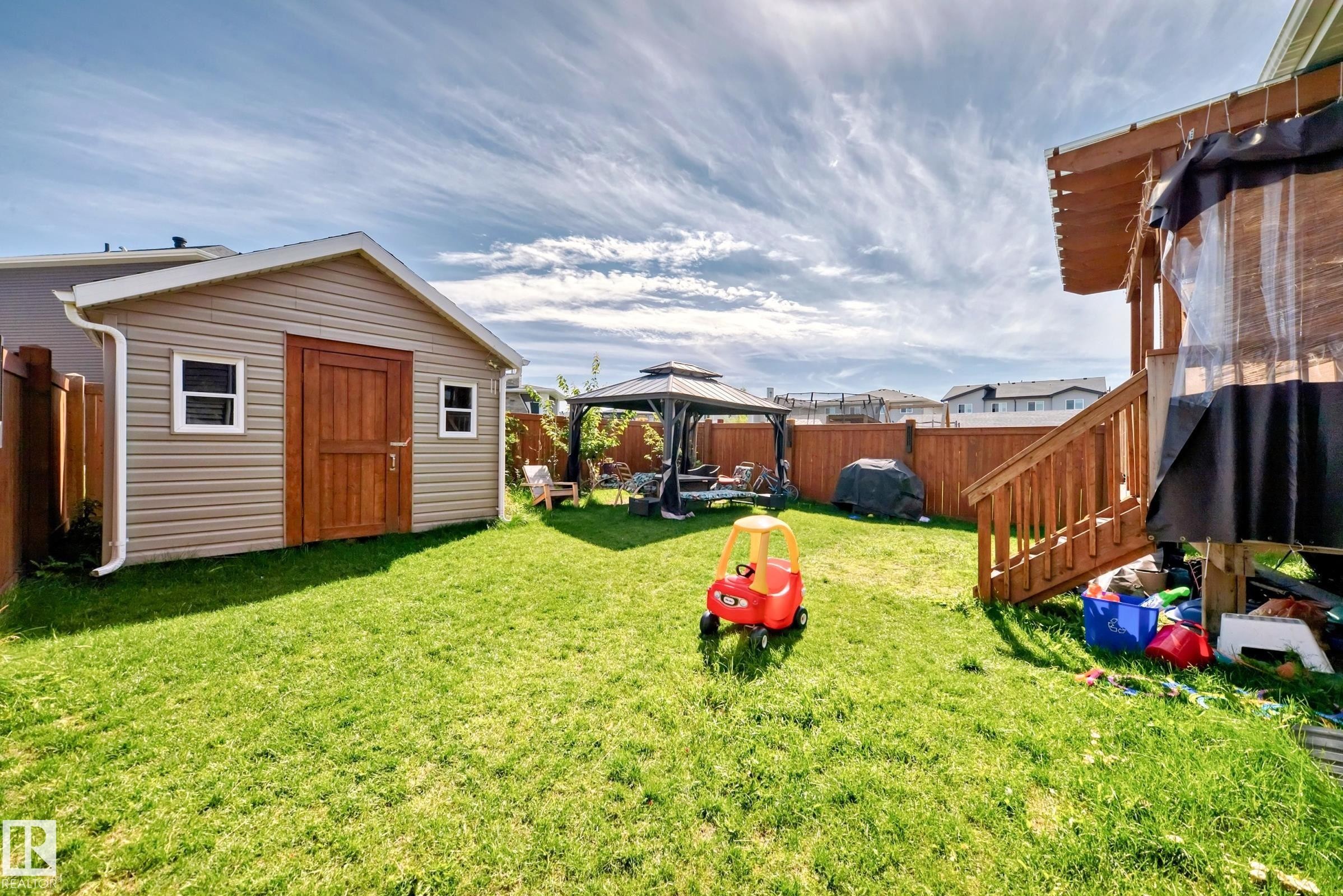 Expansive backyard featuring a manicured lawn, a detached storage shed with siding, a wooden privacy fence, a covered patio with wooden steps, and a gazebo - 4155 Charles Link, Edmonton, AB - Outdoor With Exterior