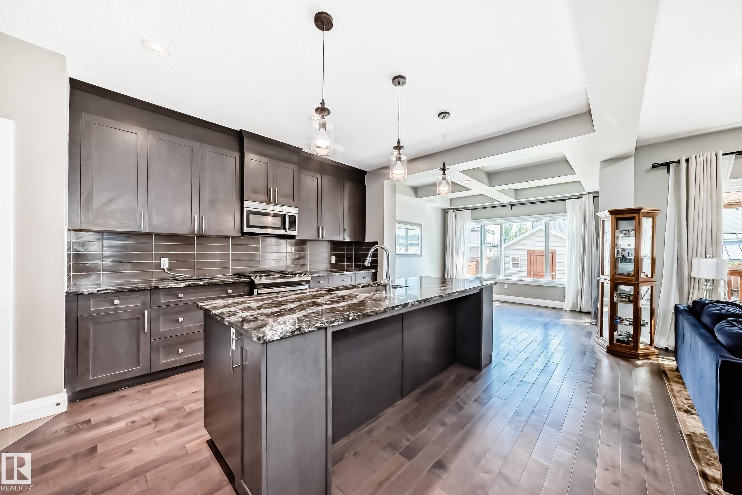 Modern kitchen featuring dark cabinetry, stone countertops, stainless steel appliances, and a tile backsplash - 4155 Charles Link, Edmonton, AB - Indoor Photo Showing Kitchen With Upgraded Kitchen
