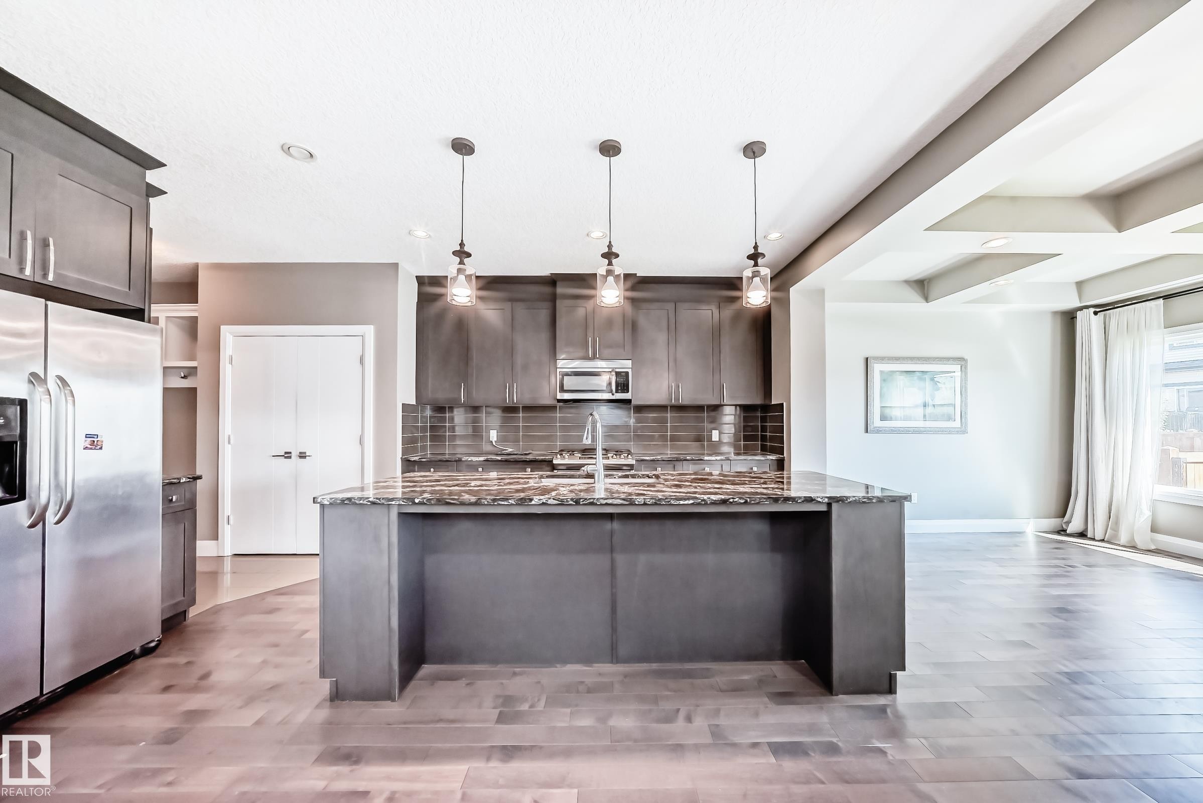 Modern kitchen featuring a large central island with a stone countertop, dark wood-finish cabinetry, stainless steel appliances, and pendant lighting - 4155 Charles Link, Edmonton, AB - Indoor Photo Showing Kitchen With Upgraded Kitchen