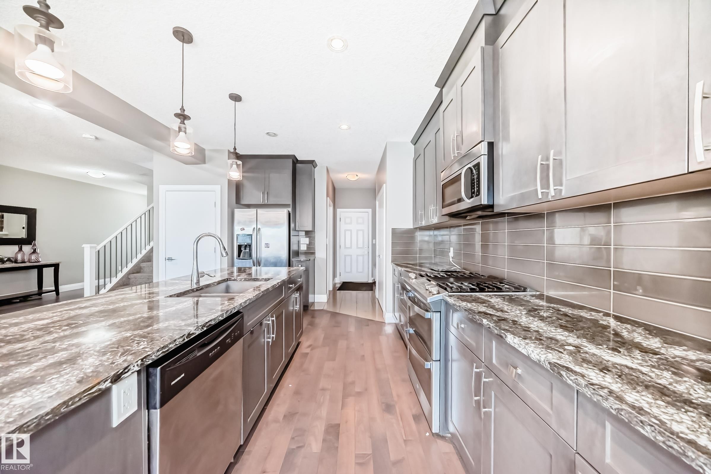 Modern kitchen featuring wood-finish flooring, stone countertops, stainless steel appliances, a tile backsplash, and contemporary pendant lighting - 4155 Charles Link, Edmonton, AB - Indoor Photo Showing Kitchen With Double Sink With Upgraded Kitchen