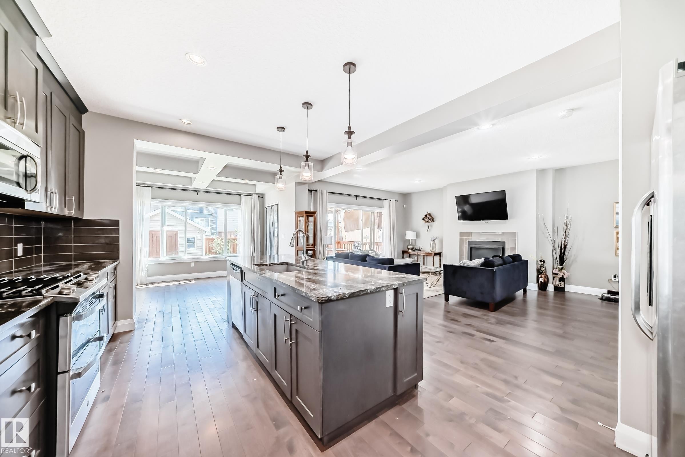 Open-concept kitchen featuring an island with a sink and pendant lighting, dark wood-finish flooring, stainless steel appliances, and dark cabinetry - 4155 Charles Link, Edmonton, AB - Indoor Photo Showing Kitchen With Upgraded Kitchen