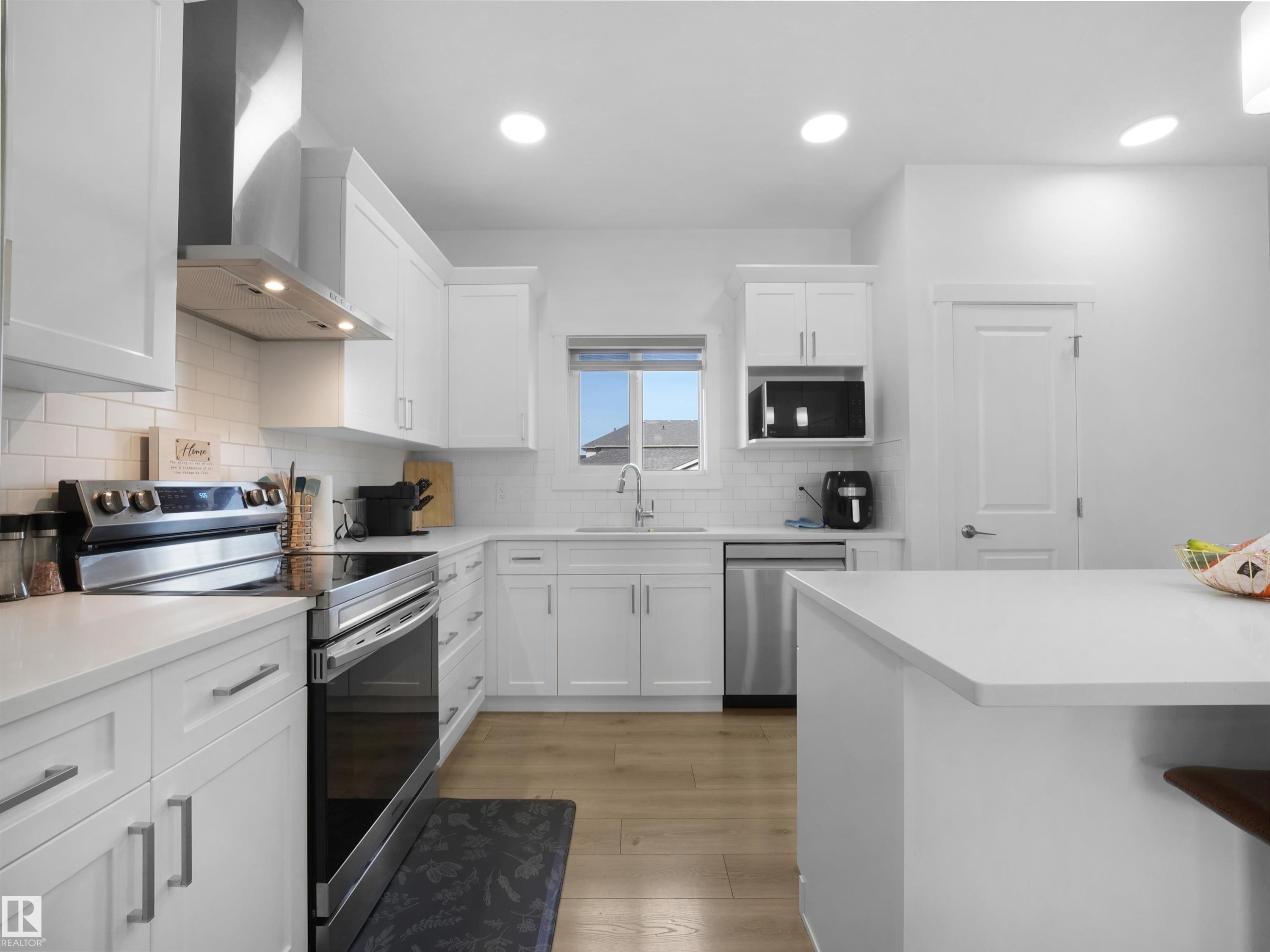 Modern kitchen featuring white shaker cabinetry, stainless steel appliances, light countertops, and wood-finish flooring - 30 Hope Cm, Spruce Grove, AB - Indoor Photo Showing Kitchen With Upgraded Kitchen