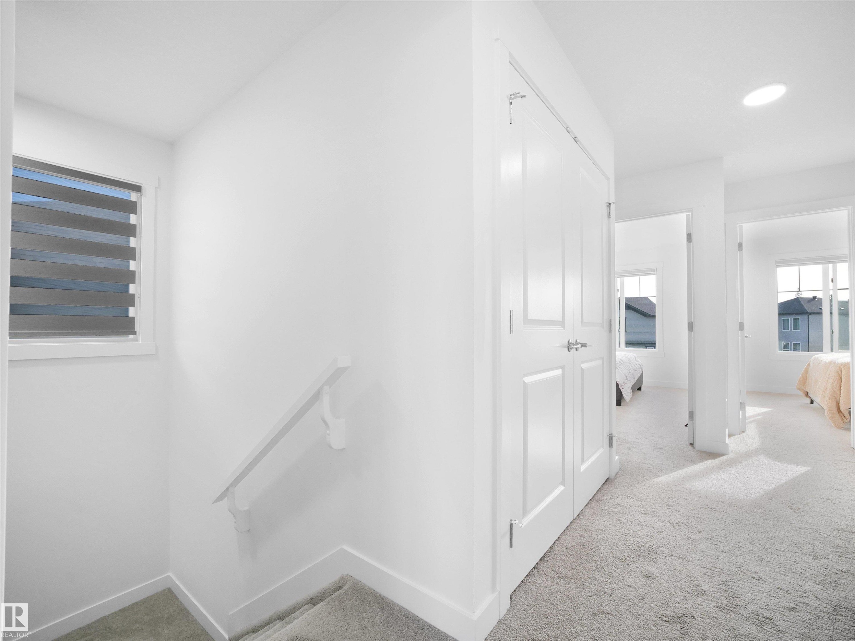Upper-level hallway with white paneled doors, light grey carpet, and a large window featuring horizontal blinds - 30 Hope Cm, Spruce Grove, AB - Indoor Photo Showing Other Room