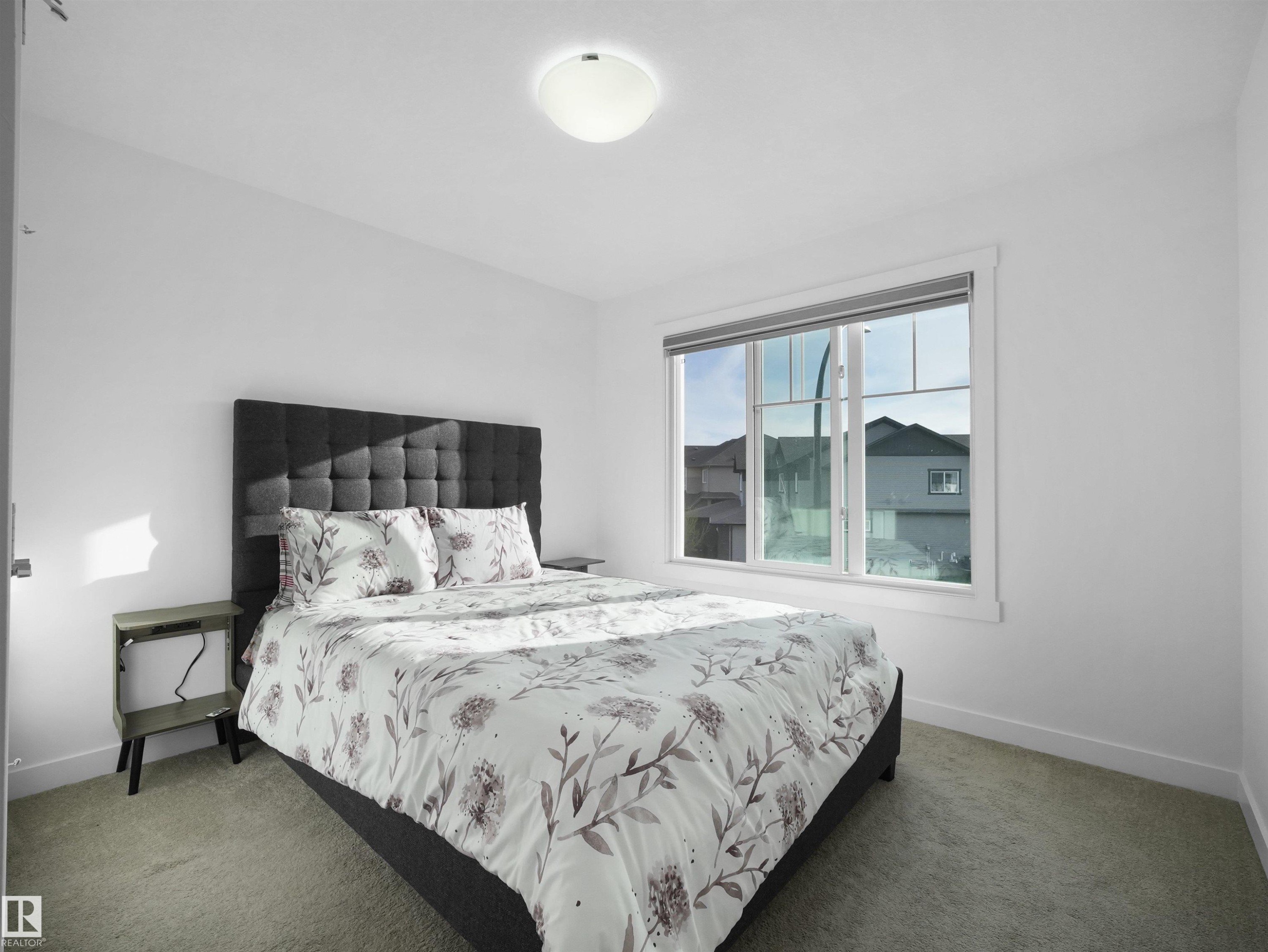 Bedroom featuring a large window, neutral wall paint, and light-colored carpet flooring - 30 Hope Cm, Spruce Grove, AB - Indoor Photo Showing Bedroom