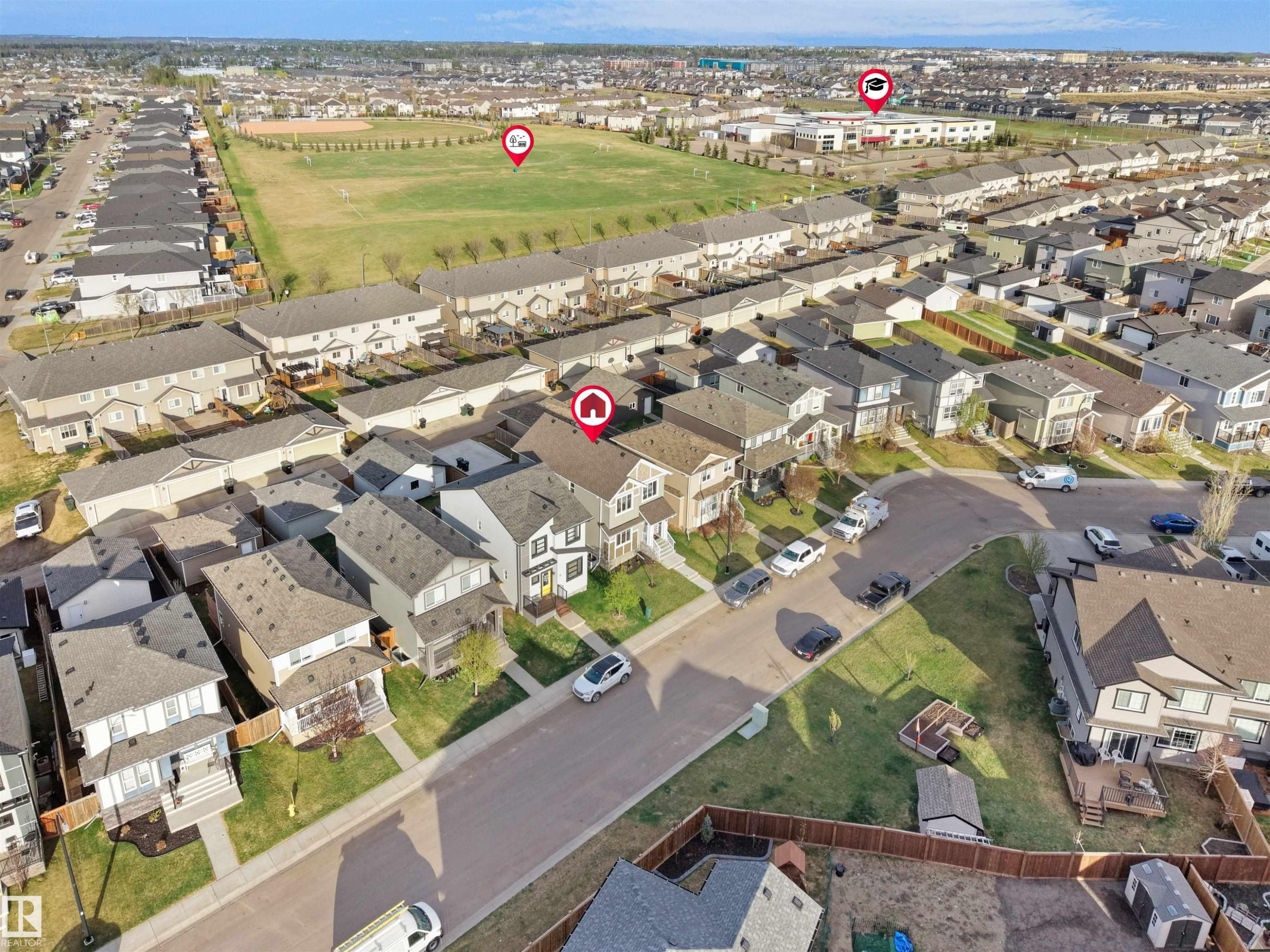 Aerial view of a residential neighborhood with detached homes, featuring street parking, a central green space, and visible community buildings - 30 Hope Cm, Spruce Grove, AB - Outdoor With View