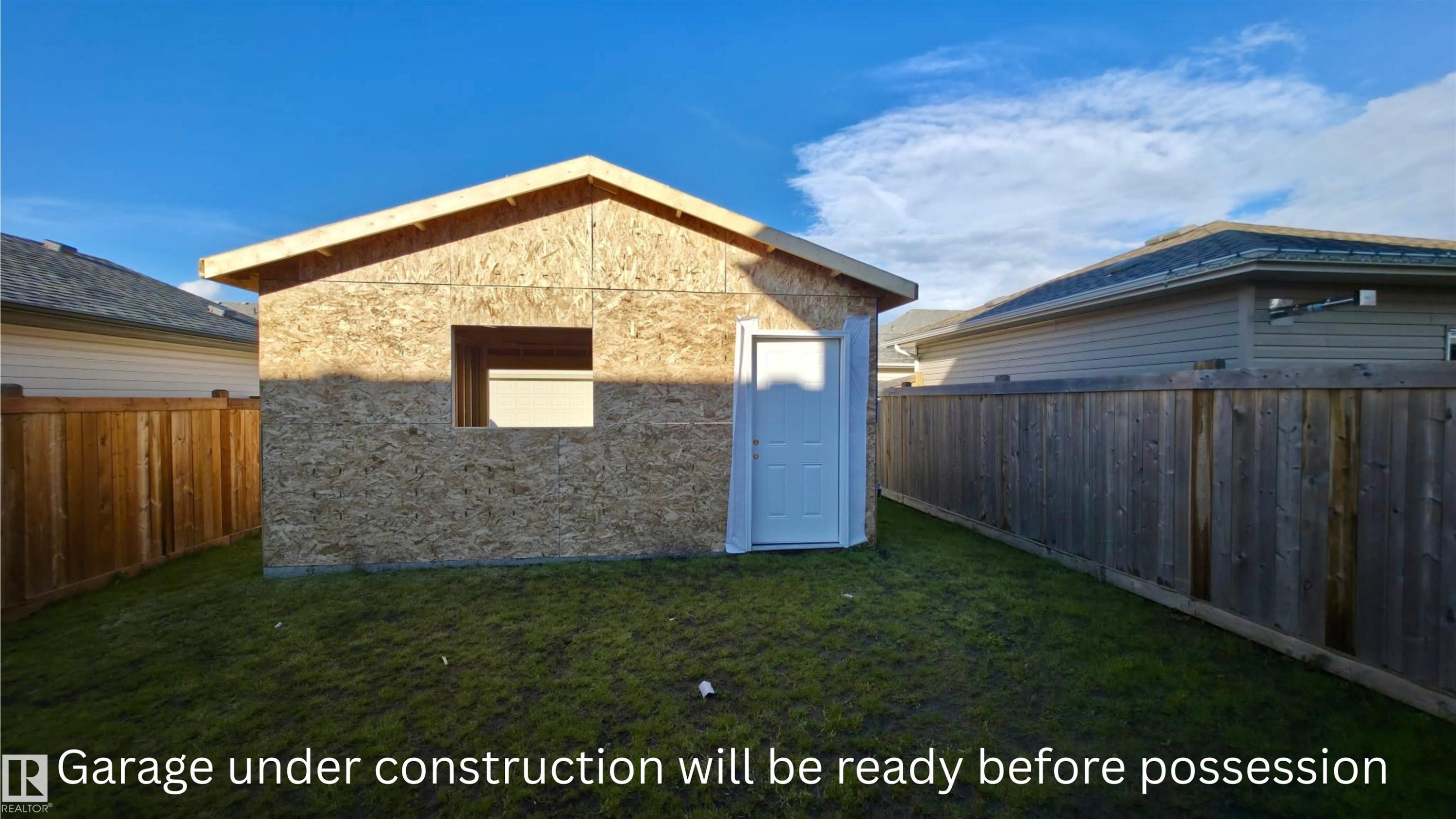 New construction garage with a single entry door and an open window frame, situated on a grassy lot - 30 Hope Cm, Spruce Grove, AB -