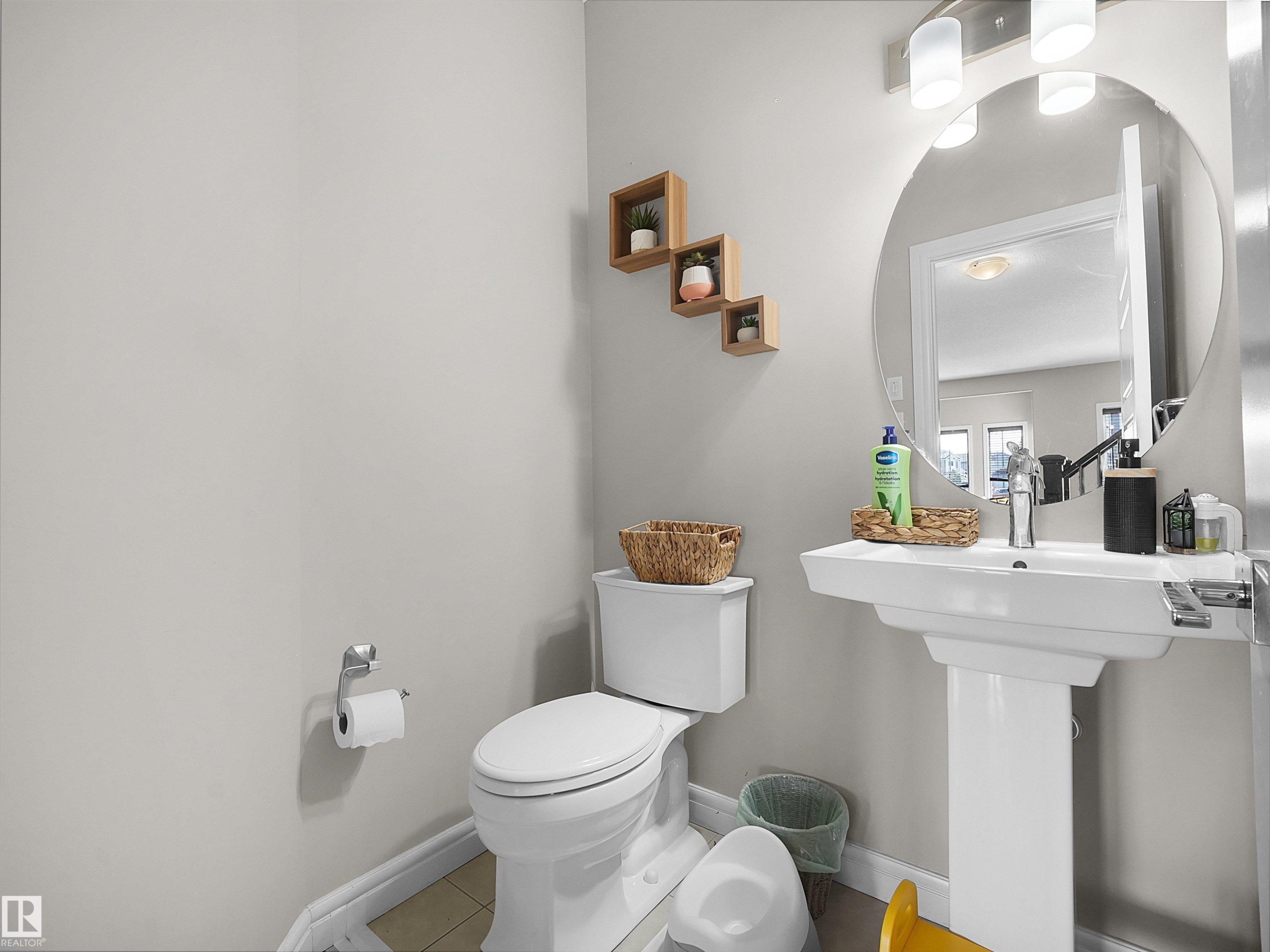 Pedestal sink with single-handle faucet, circular mirror, and modern vanity lighting - 3247 15 Avenue Nw, Edmonton, AB - Indoor Photo Showing Bathroom