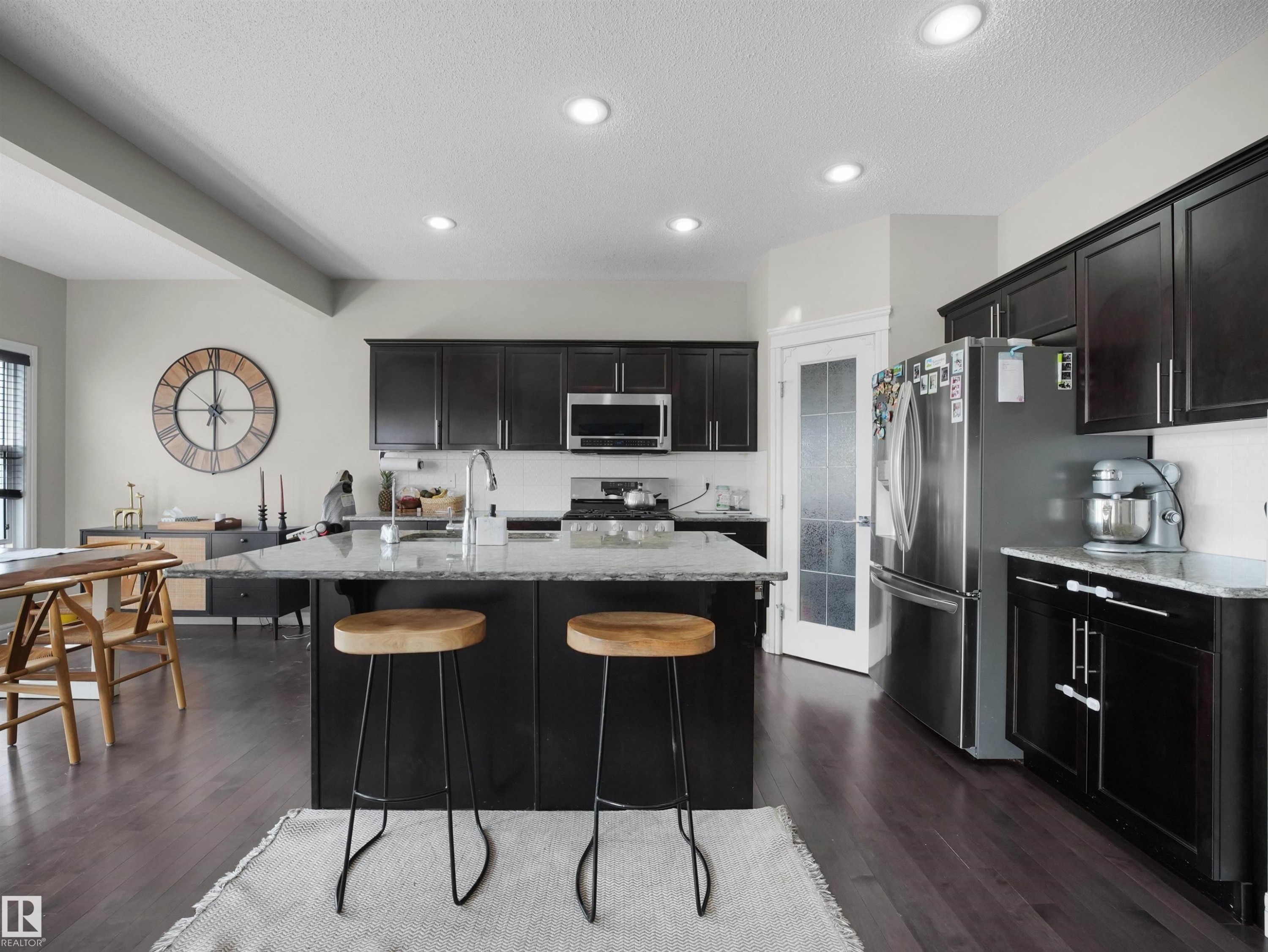 Kitchen featuring dark wood-finish cabinetry, stainless steel appliances, recessed ceiling lighting, a central island with a light-toned countertop, and wood-finish flooring - 3247 15 Avenue Nw, Edmonton, AB - Indoor Photo Showing Kitchen With Upgraded Kitchen