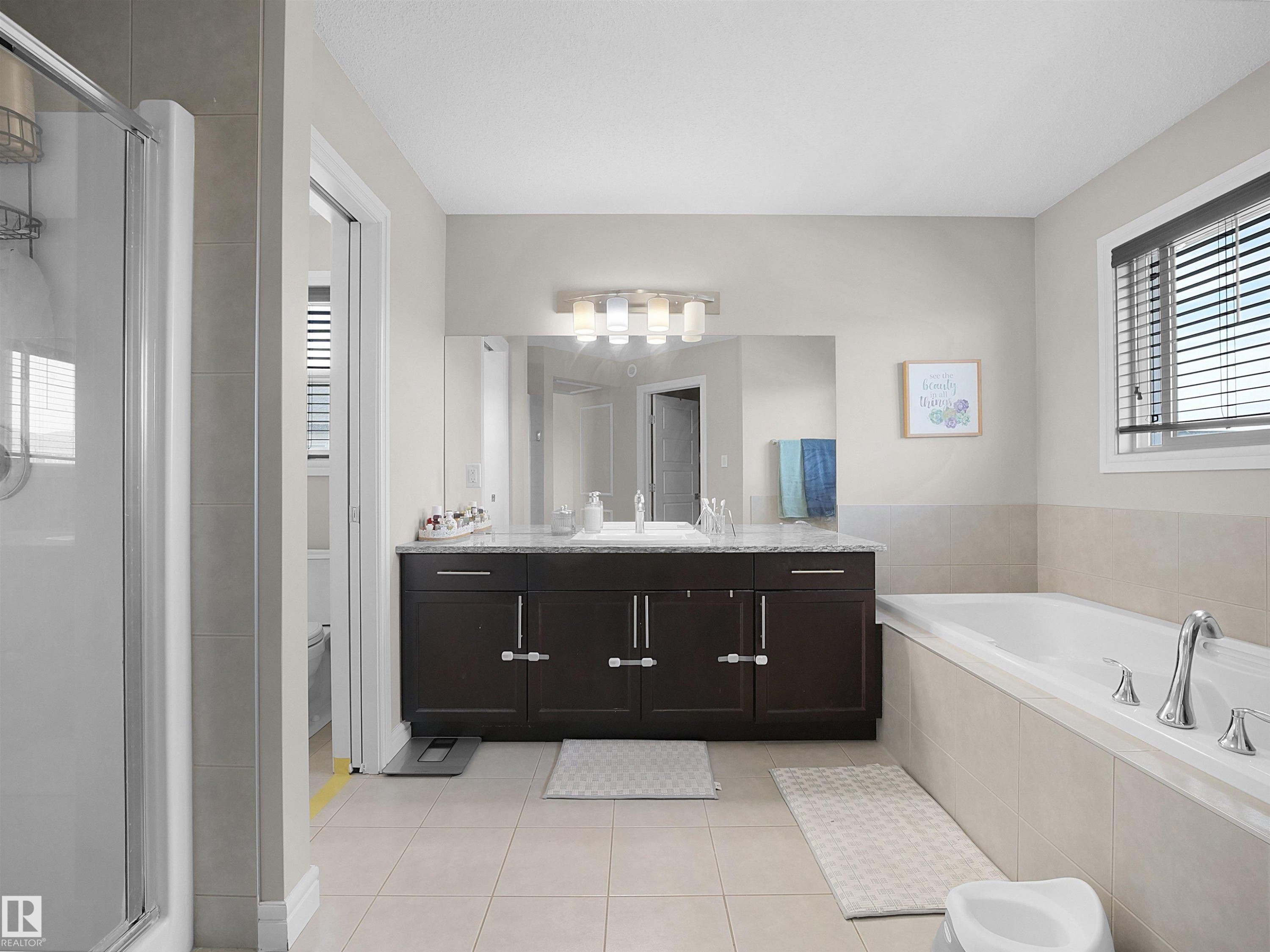 Spacious bathroom featuring a dual vanity with a granite-style countertop, a built-in bathtub, a separate shower enclosure, and tiled flooring - 3247 15 Avenue Nw, Edmonton, AB - Indoor Photo Showing Bathroom