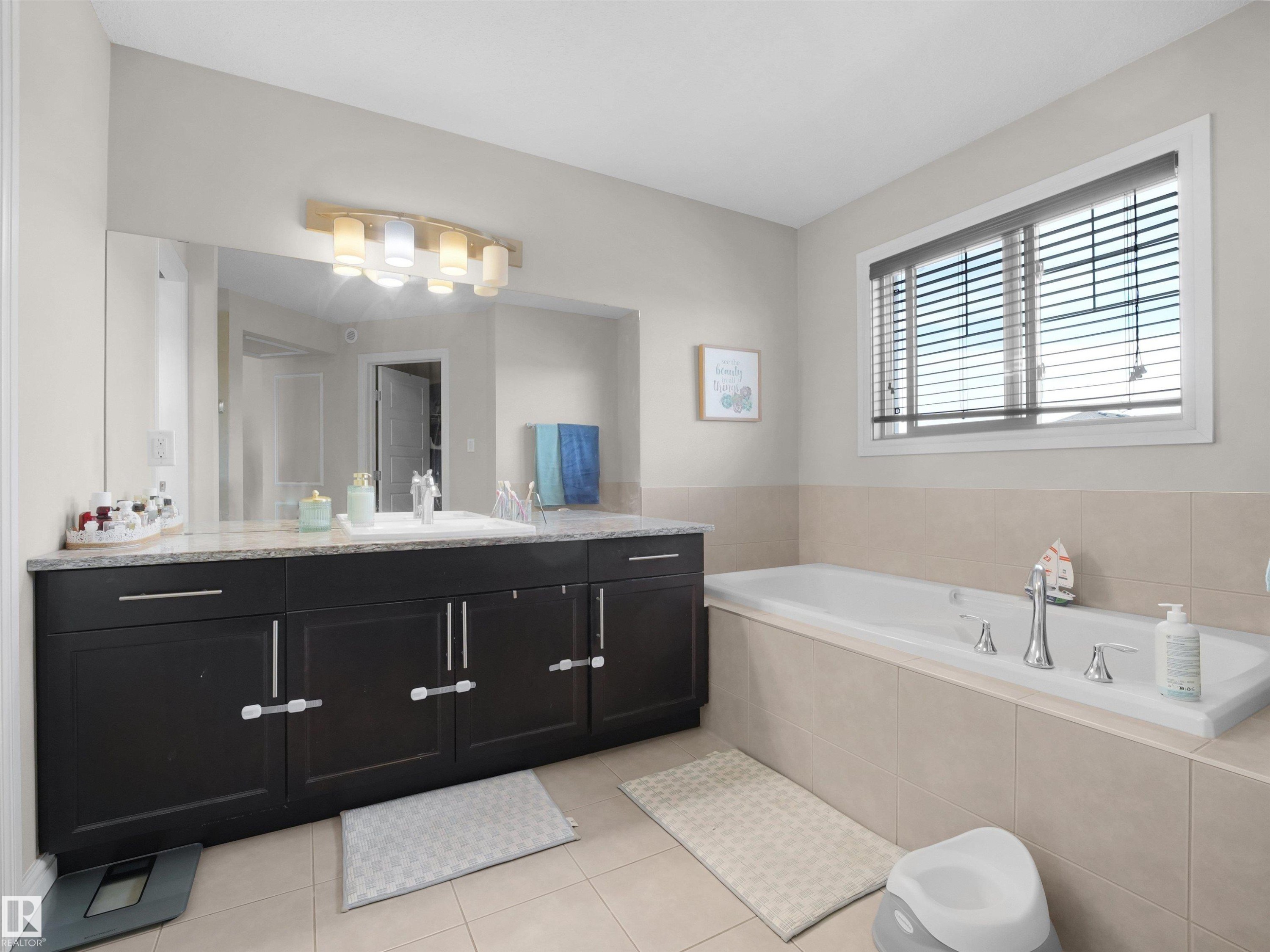 Spacious bathroom featuring a dark wood-finish double vanity with a light-toned countertop, a large mirror, and an overhead vanity light fixture - 3247 15 Avenue Nw, Edmonton, AB - Indoor Photo Showing Bathroom