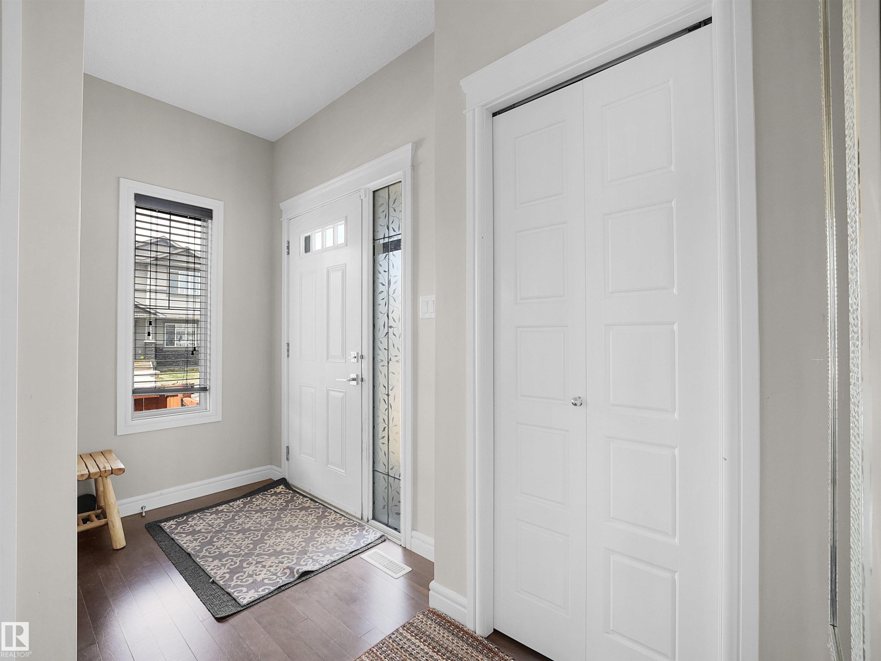 Entryway featuring a white paneled door with decorative sidelight, wood-finish flooring, a white-trimmed window, and a built-in closet with bi-fold doors - 3247 15 Avenue Nw, Edmonton, AB - Indoor Photo Showing Other Room