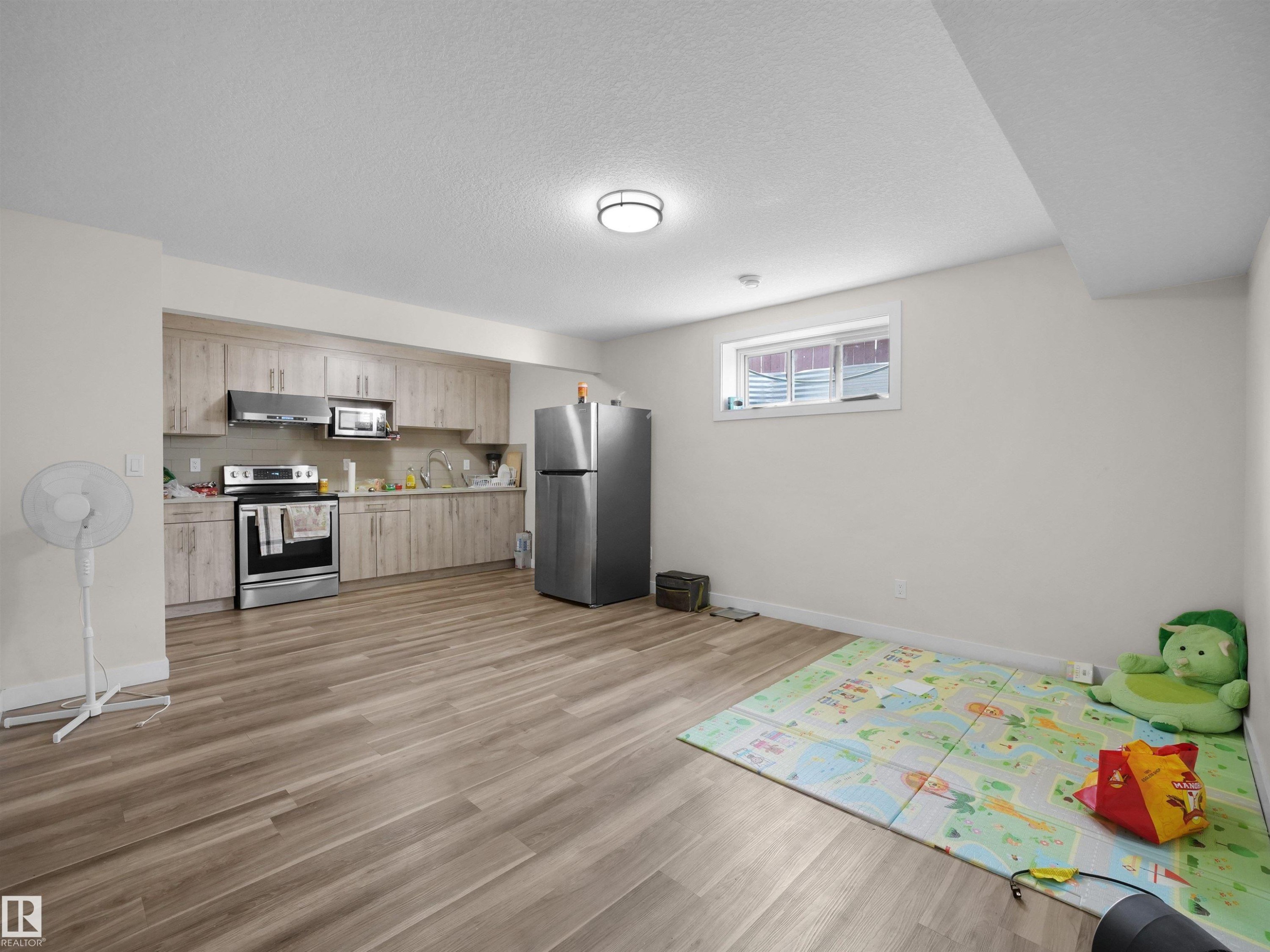 Open-concept living space with wood-finish flooring, a full kitchen featuring light wood-tone cabinetry, stainless steel appliances, and a window - 3247 15 Avenue Nw, Edmonton, AB - Indoor Photo Showing Kitchen