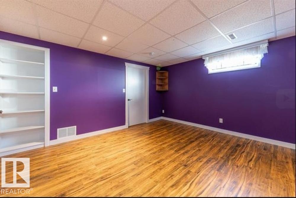 Spacious room featuring wood-finish flooring, vibrant wall color, a drop-ceiling with recessed lighting, integrated shelving, and a built-in corner shelf unit - 1412 63 Street, Edmonton, AB - Indoor