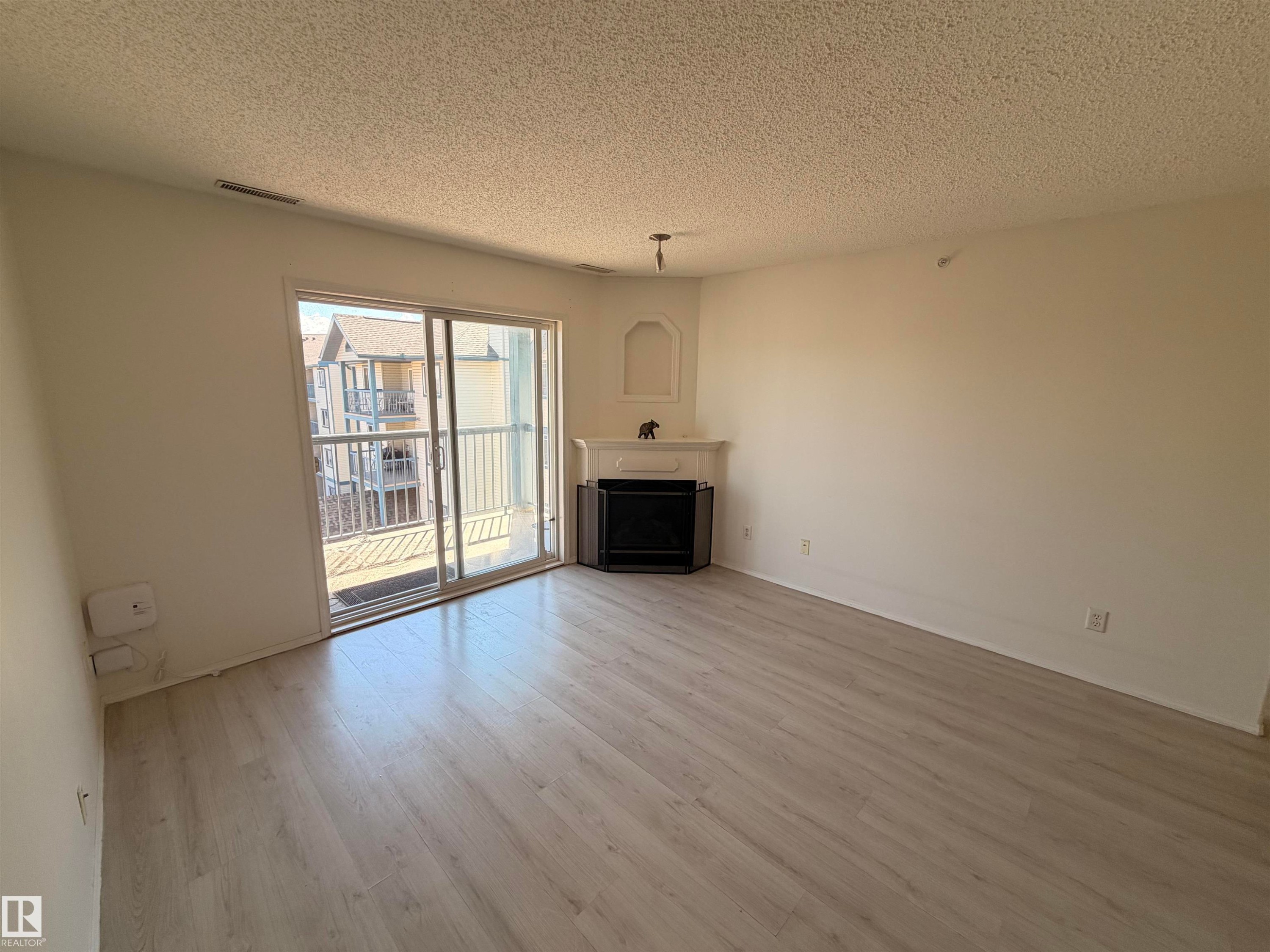 Living area featuring light wood-finish flooring, white walls, and a corner fireplace with a decorative mantel and niche - #424 16303 95 St Nw, Edmonton, AB - Indoor Photo Showing Living Room With Fireplace