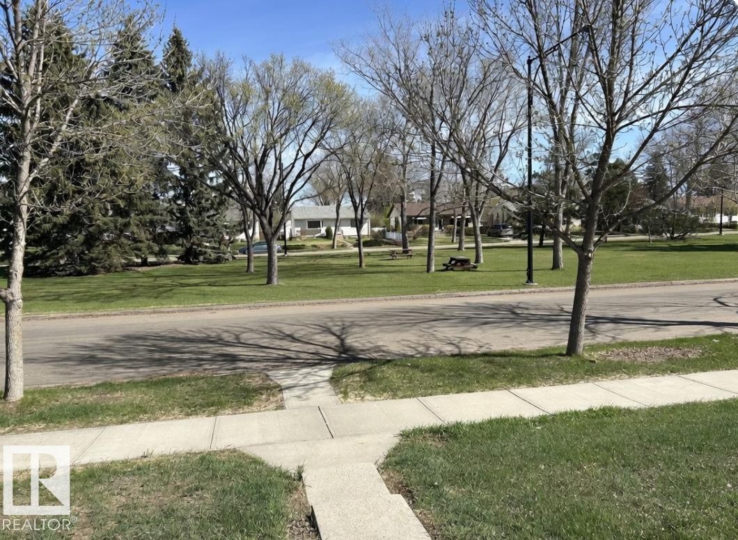 Manicured green lawn with a concrete sidewalk and asphalt street, bordered by deciduous trees and evergreen shrubs - 13543 124A Avenue, Edmonton, AB - Outdoor With View