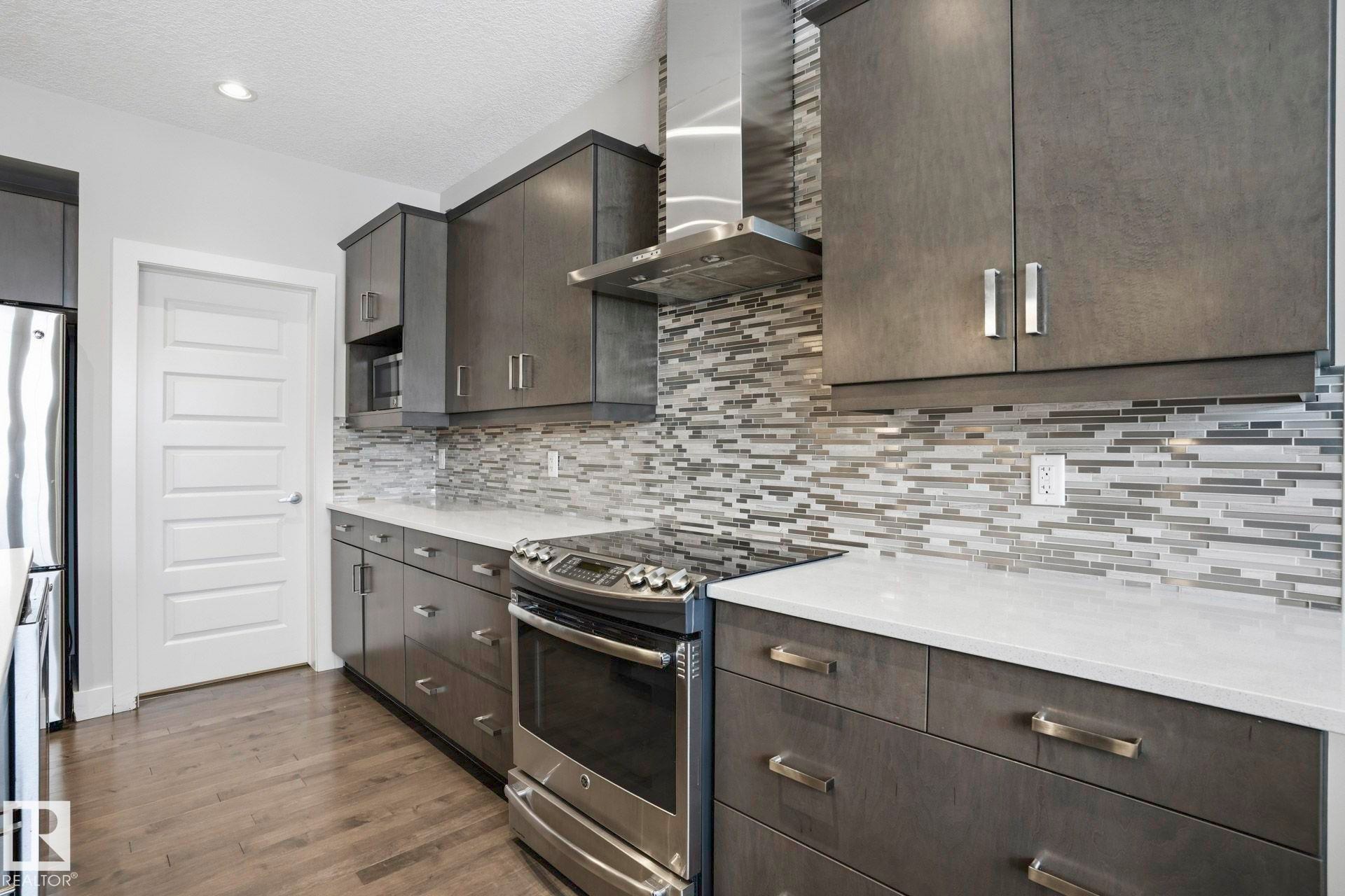 Kitchen featuring stainless steel appliances, a textured ceiling, dark wood-style floors, light stone countertops, and decorative backsplash - 1915 77 Street, Edmonton, AB - Indoor Photo Showing Kitchen With Upgraded Kitchen