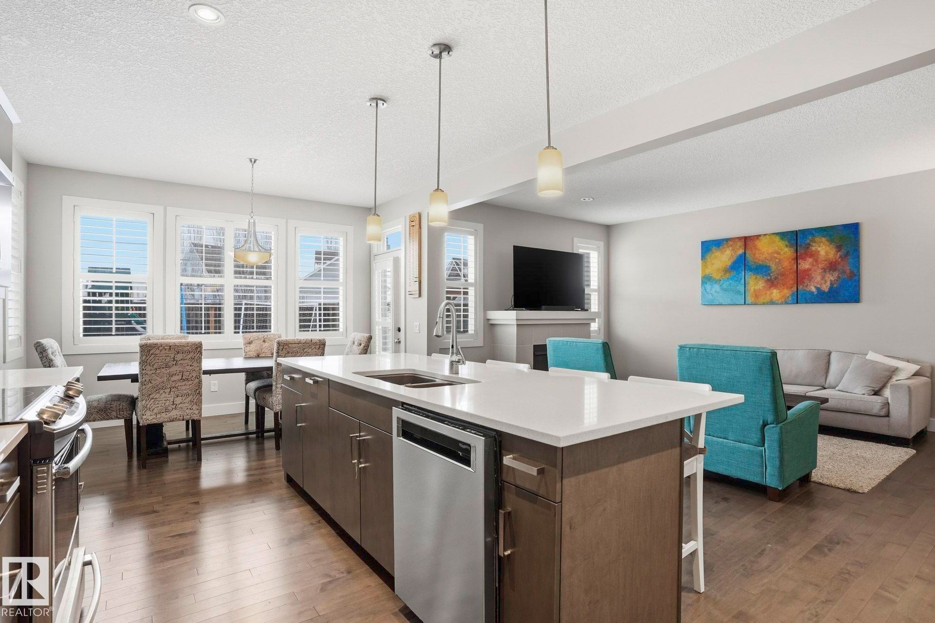 Kitchen with open floor plan, dark wood finish cabinets, stainless steel appliances, hanging light fixtures, and a textured ceiling - 1915 77 Street, Edmonton, AB - Indoor Photo Showing Kitchen With Double Sink