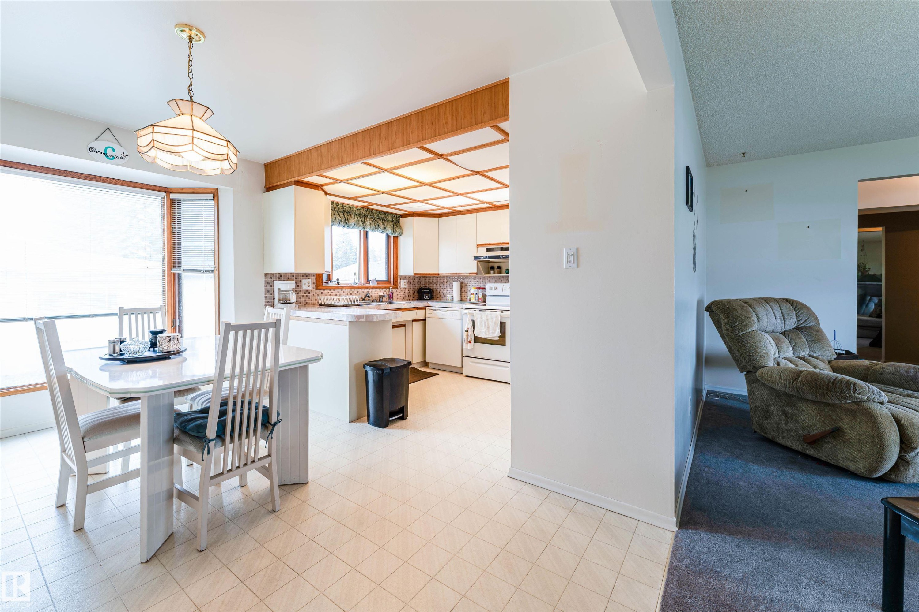 Kitchen and dining area featuring a bay window, white cabinetry, light-toned tiled flooring, and a recessed ceiling with wood-finish trim - 13231 74 Street, Edmonton, AB - Indoor Photo Showing Other Room
