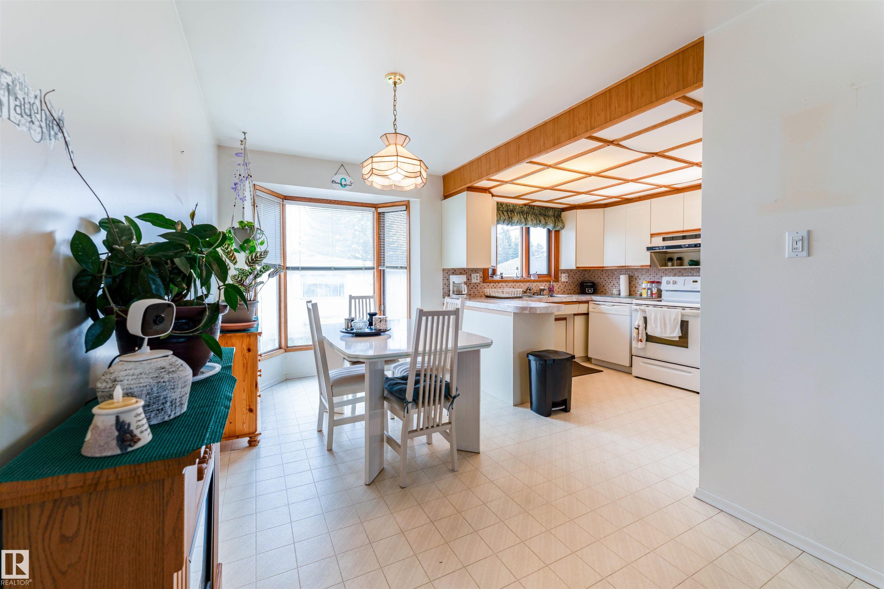 Kitchen and dining area featuring a bay window, a coffered ceiling with wood-finish trim, white cabinetry, a built-in kitchen island, and tiled flooring - 13231 74 Street, Edmonton, AB - Indoor