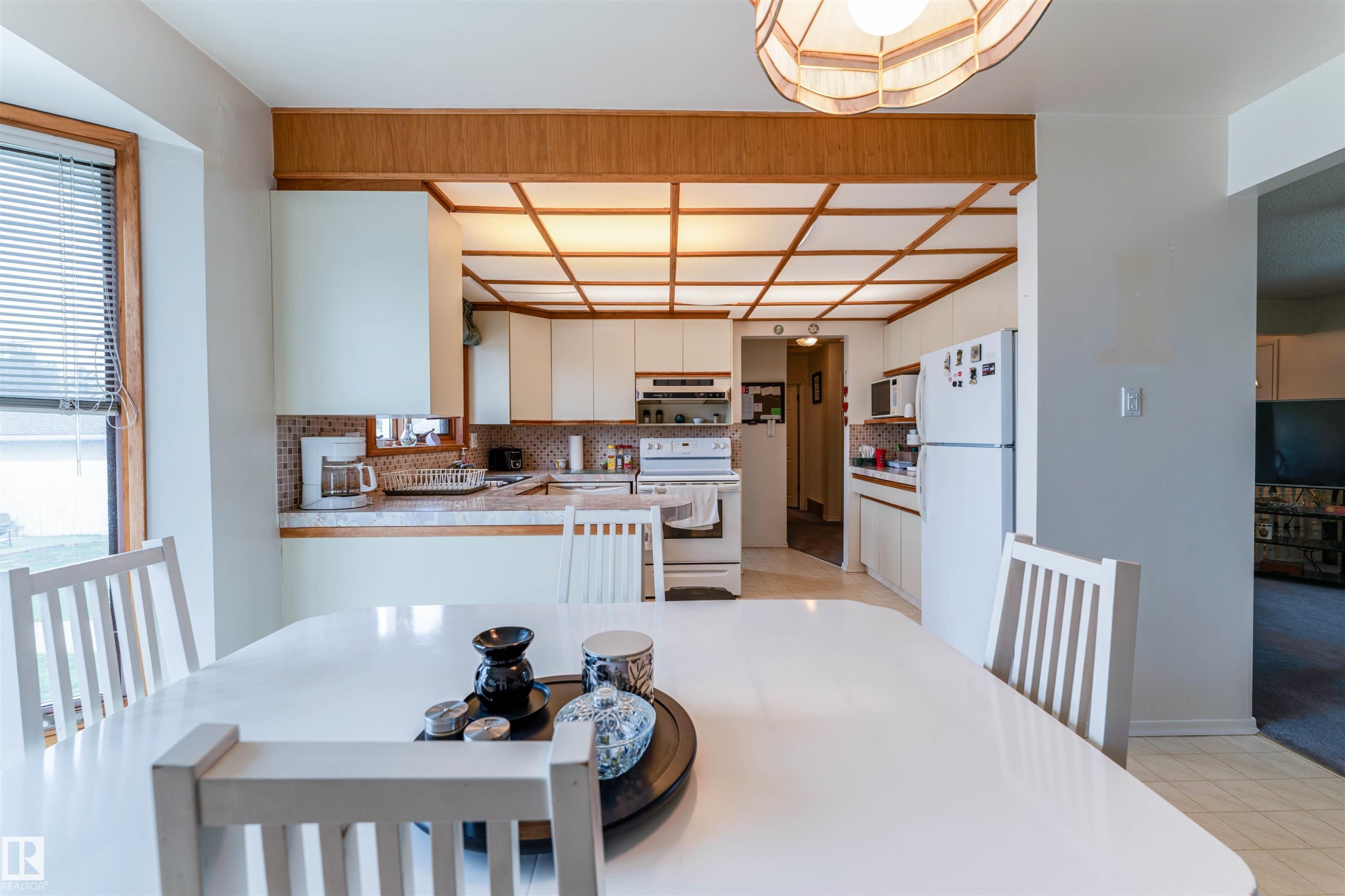 Kitchen and dining area featuring a tray ceiling with wood-finish trim, white cabinetry, a tiled backsplash, and light-colored appliances - 13231 74 Street, Edmonton, AB - Indoor Photo Showing Other Room