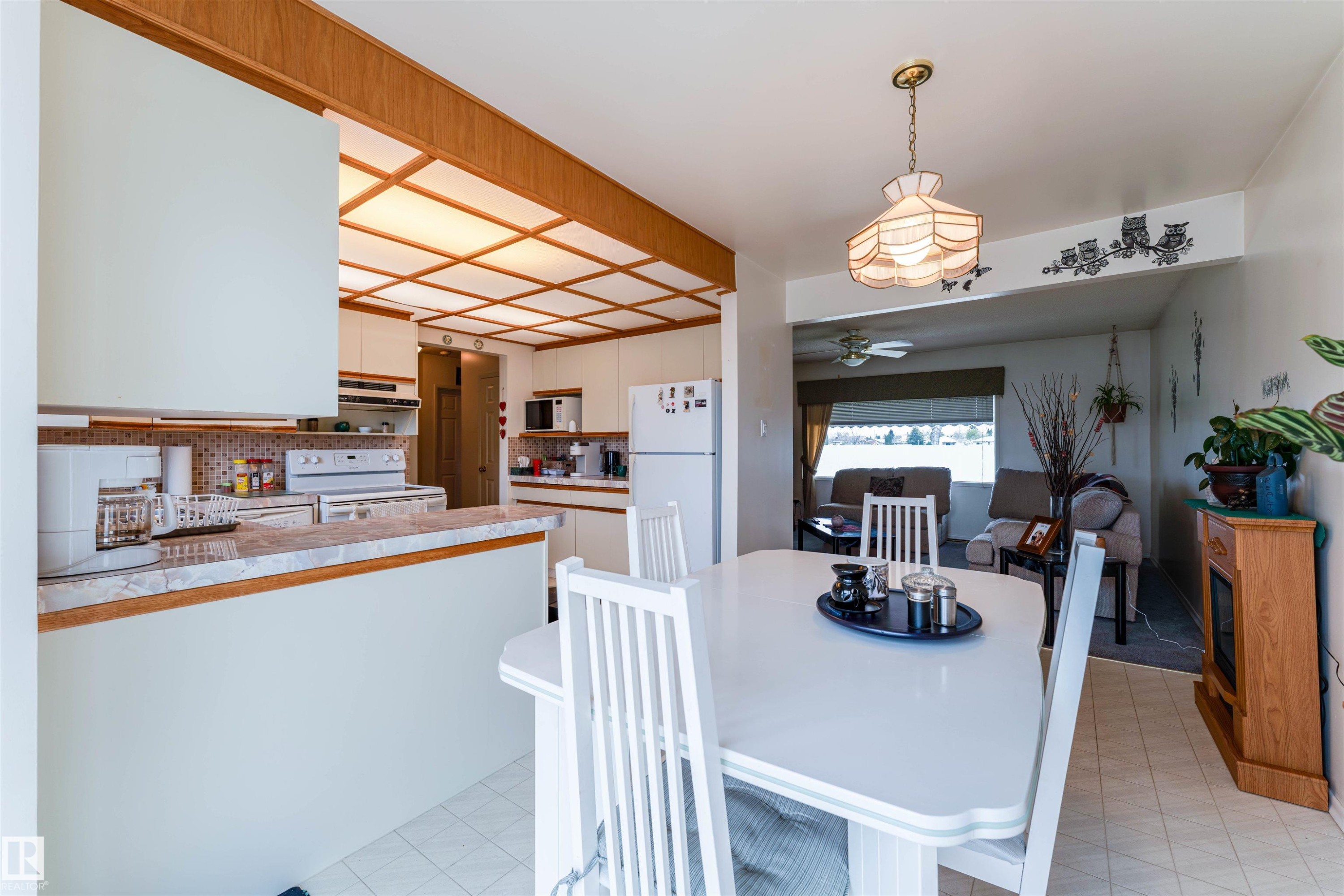 Kitchen and dining area featuring a breakfast bar with a light-toned countertop, white cabinetry, a coffered ceiling with integrated lighting, and white tile flooring - 13231 74 Street, Edmonton, AB - Indoor Photo Showing Dining Room