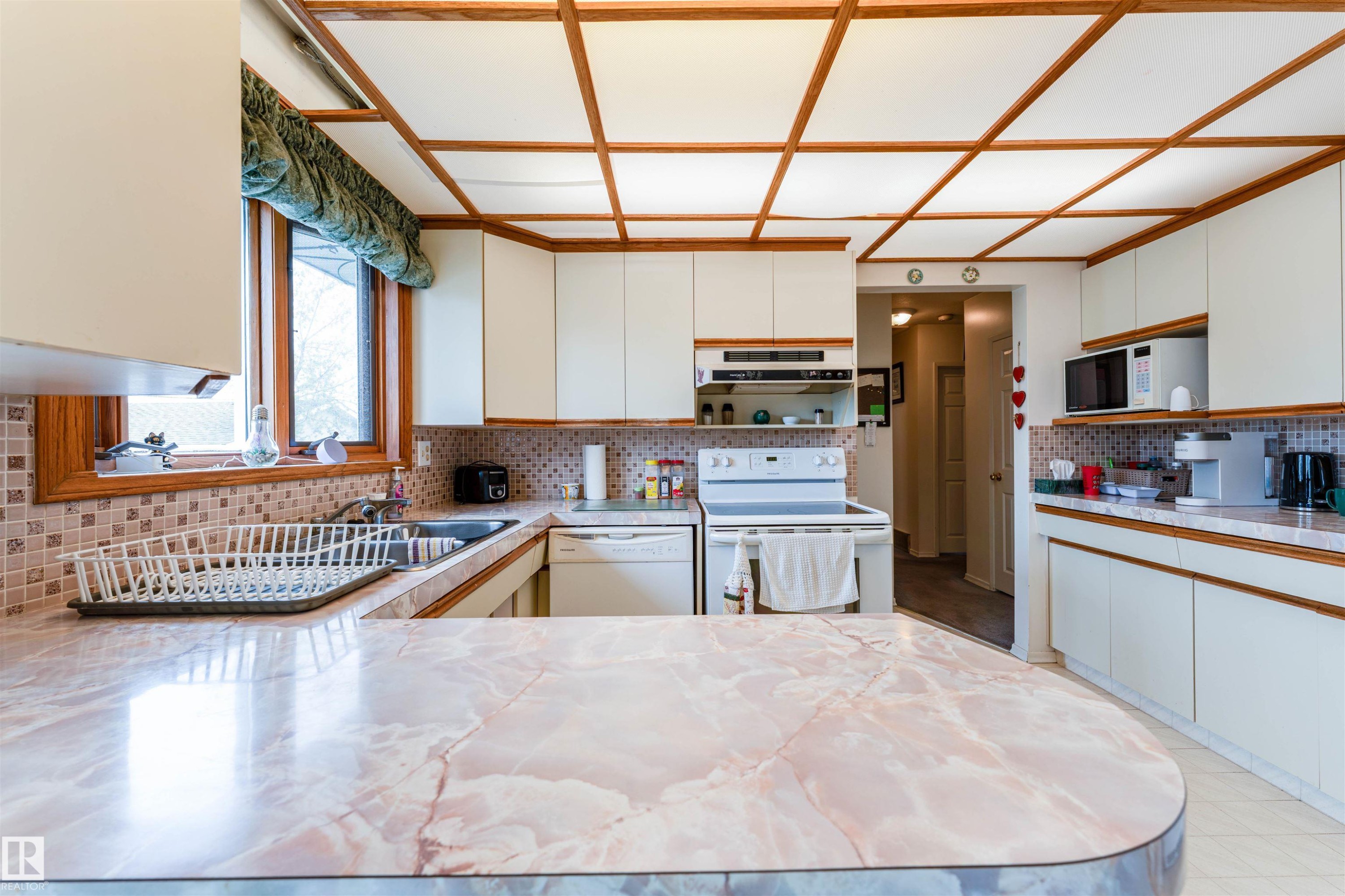Kitchen featuring a coffered ceiling, light-toned cabinetry, a mosaic tile backsplash, a stainless steel sink, and an extended countertop - 13231 74 Street, Edmonton, AB - Indoor Photo Showing Kitchen