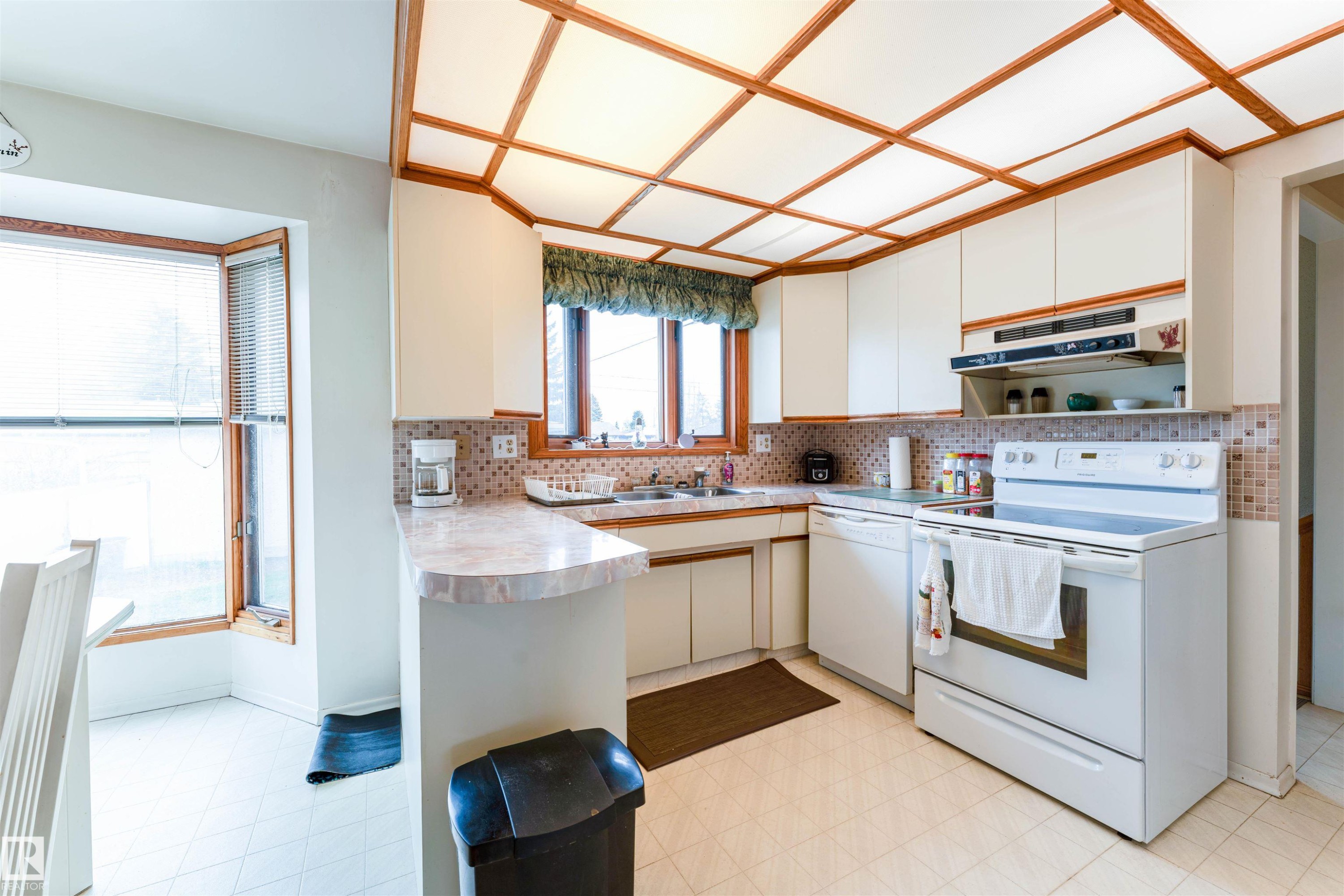 Kitchen featuring white cabinetry, white appliances, a patterned tile backsplash, and a drop ceiling with wood-finish trim - 13231 74 Street, Edmonton, AB - Indoor