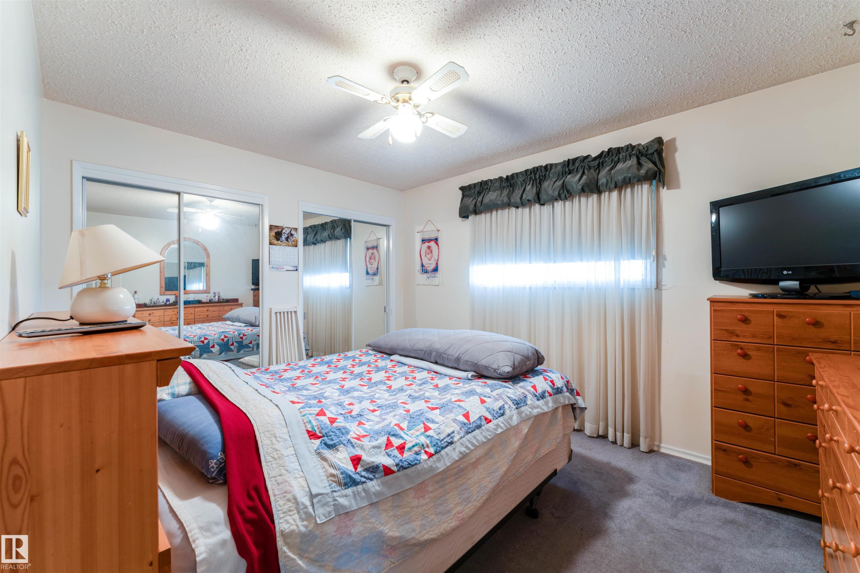 Bedroom featuring a ceiling fan with integrated lighting, mirrored sliding closet doors, and carpet flooring - 13231 74 Street, Edmonton, AB - Indoor Photo Showing Bedroom