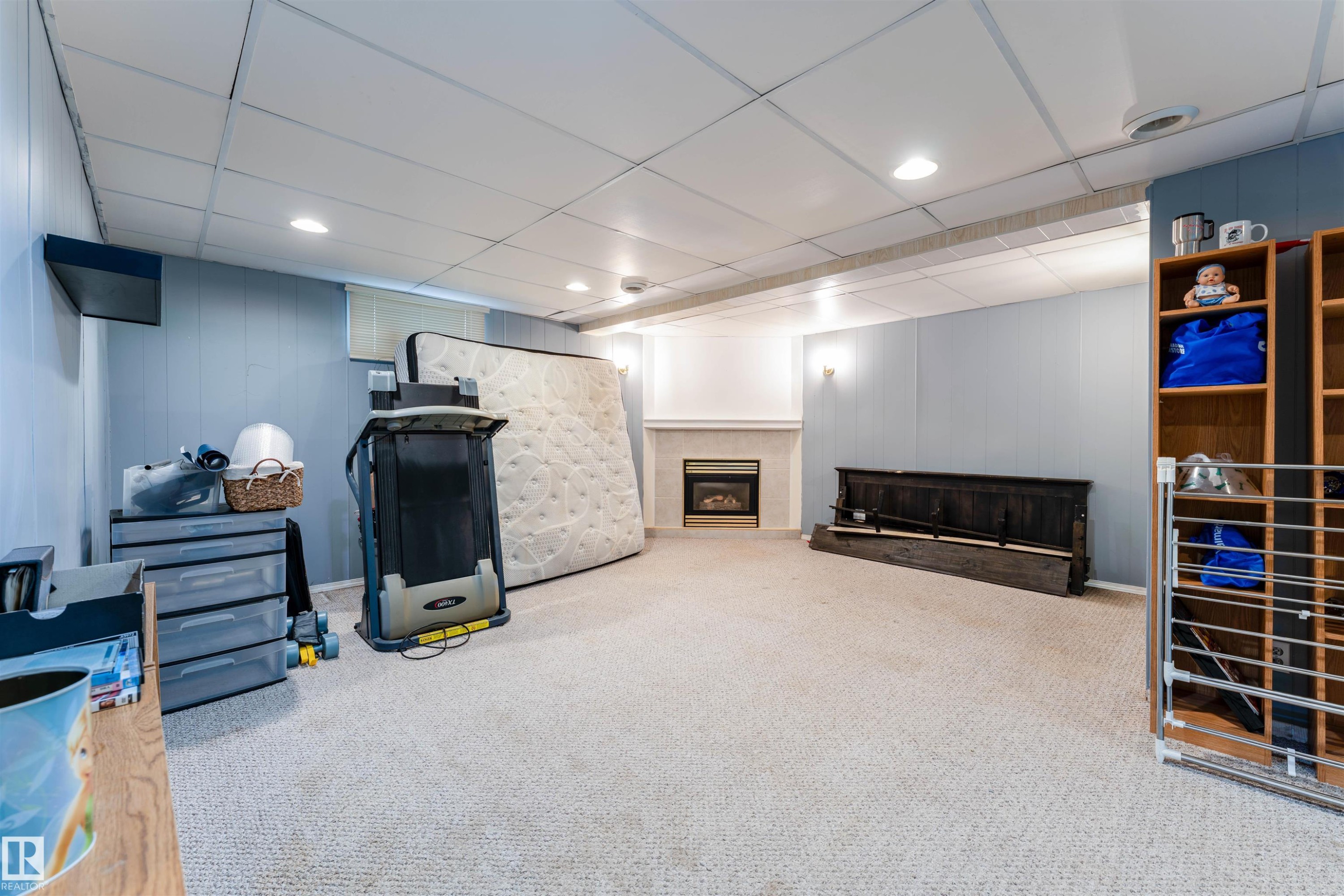 Carpeted room featuring a white panel ceiling with recessed lighting, light blue panel walls, and a fireplace with a white mantel and hearth - 13231 74 Street, Edmonton, AB - Indoor