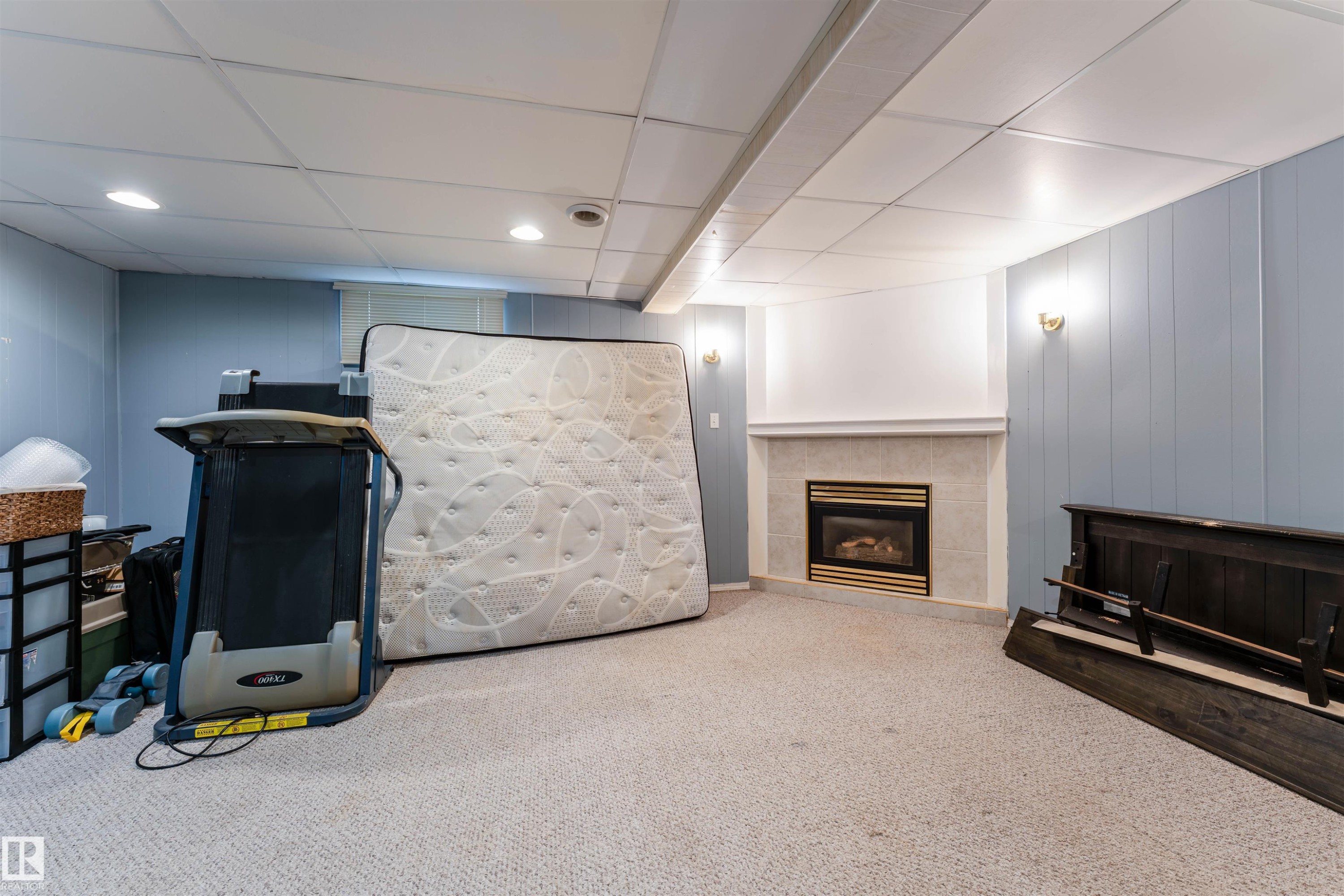 Carpeted room featuring a fireplace with a light-toned tile surround and white mantel - 13231 74 Street, Edmonton, AB - Indoor Photo Showing Other Room
