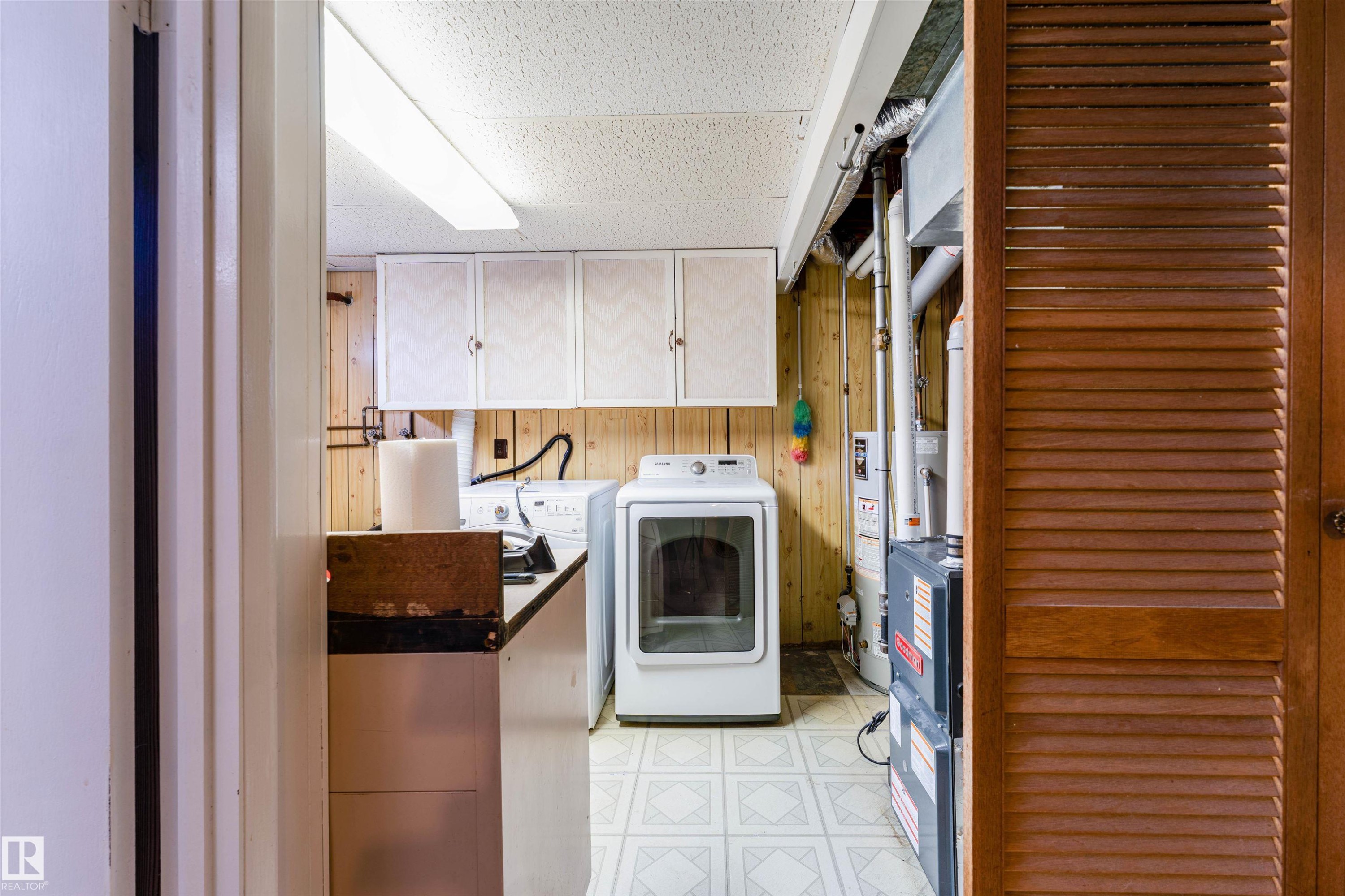 Dedicated laundry area featuring a utility sink, upper cabinetry, wood paneling, and patterned vinyl flooring - 13231 74 Street, Edmonton, AB - Indoor Photo Showing Kitchen
