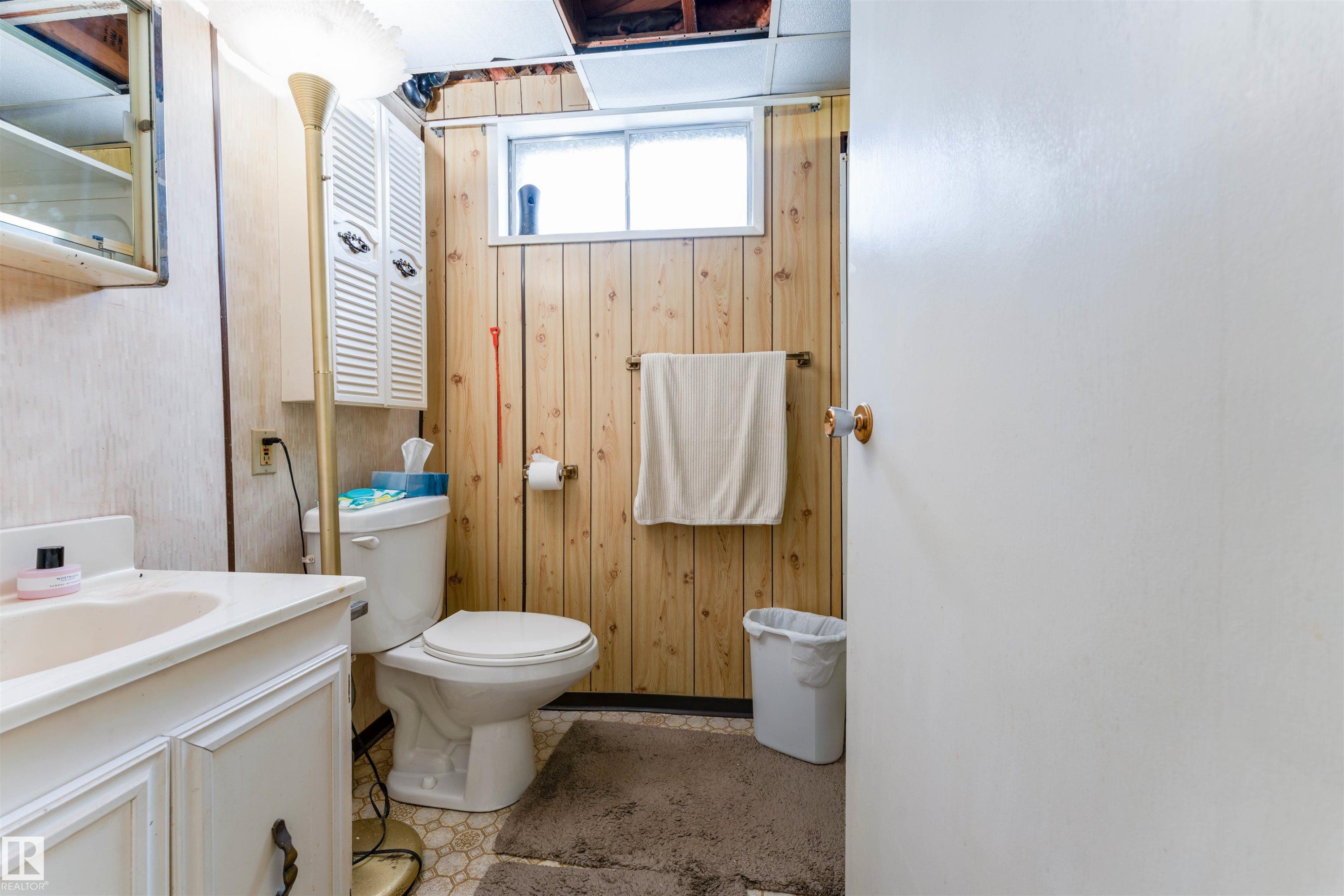 Bathroom featuring a white vanity with integrated sink, white toilet, and wood-finish wall paneling - 13231 74 Street, Edmonton, AB - Indoor Photo Showing Bathroom