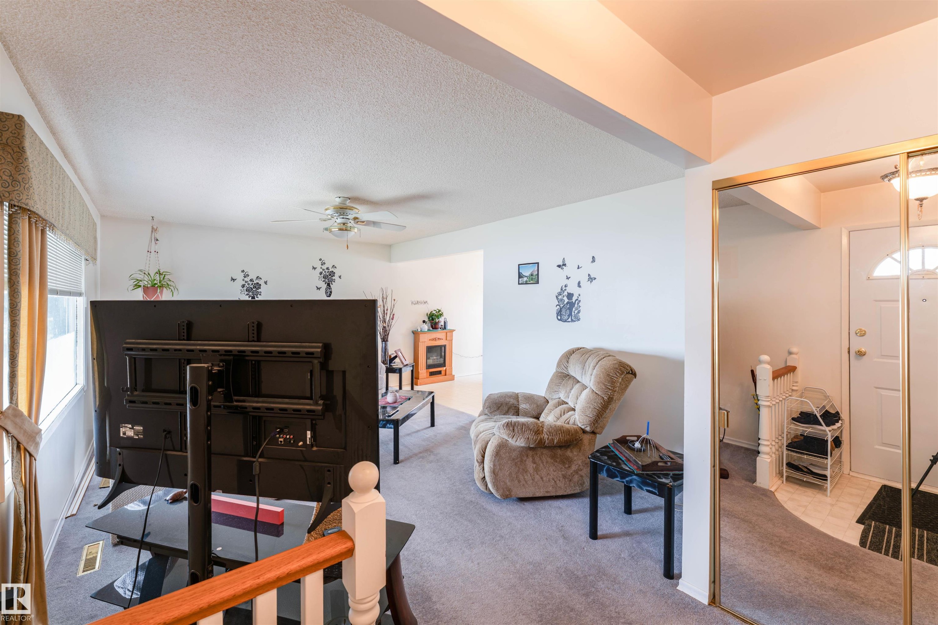 Living area featuring a ceiling fan, carpet flooring, a window with horizontal blinds, and a built-in electric fireplace - 13231 74 Street, Edmonton, AB - Indoor