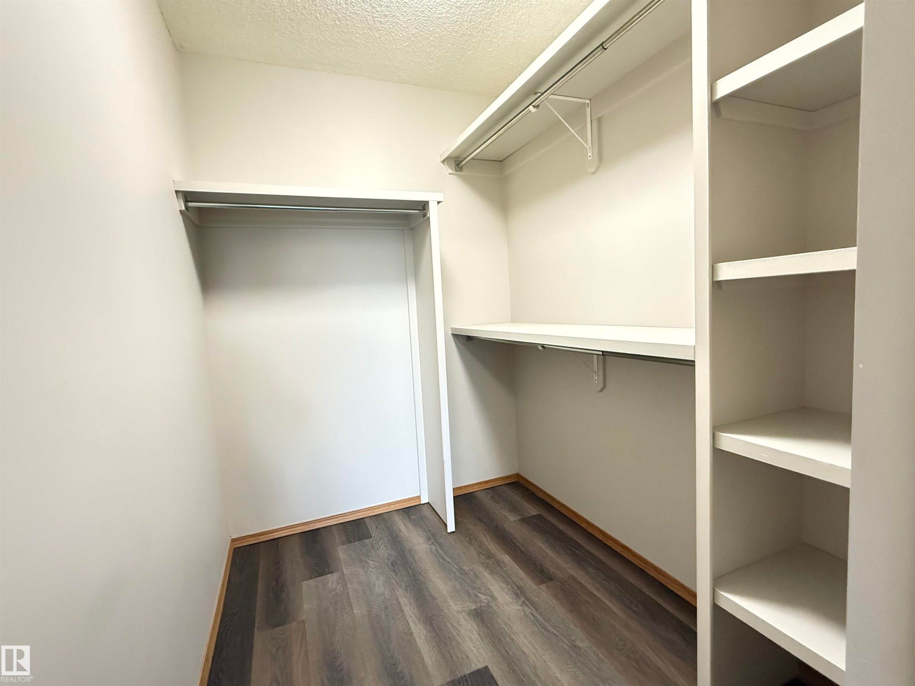 Walk-in closet featuring wood-finish flooring, white walls, built-in shelving, and multiple hanging rods - #309 10610 76 St Nw, Edmonton, AB - Indoor With Storage