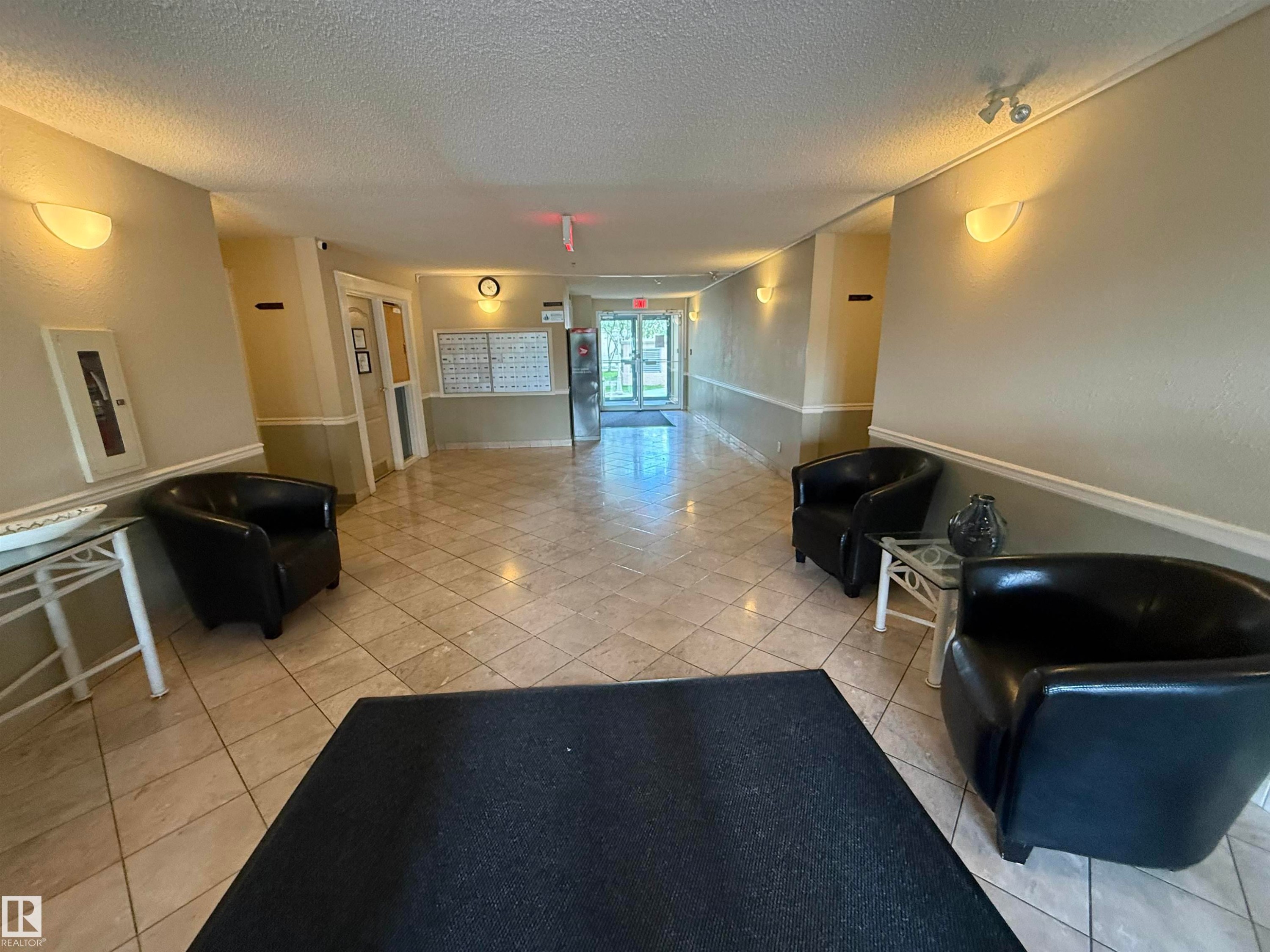 Entry foyer featuring large format tile flooring, sconce lighting, and a two-tone wall finish with chair rail molding - #309 10610 76 St Nw, Edmonton, AB - Indoor Photo Showing Other Room