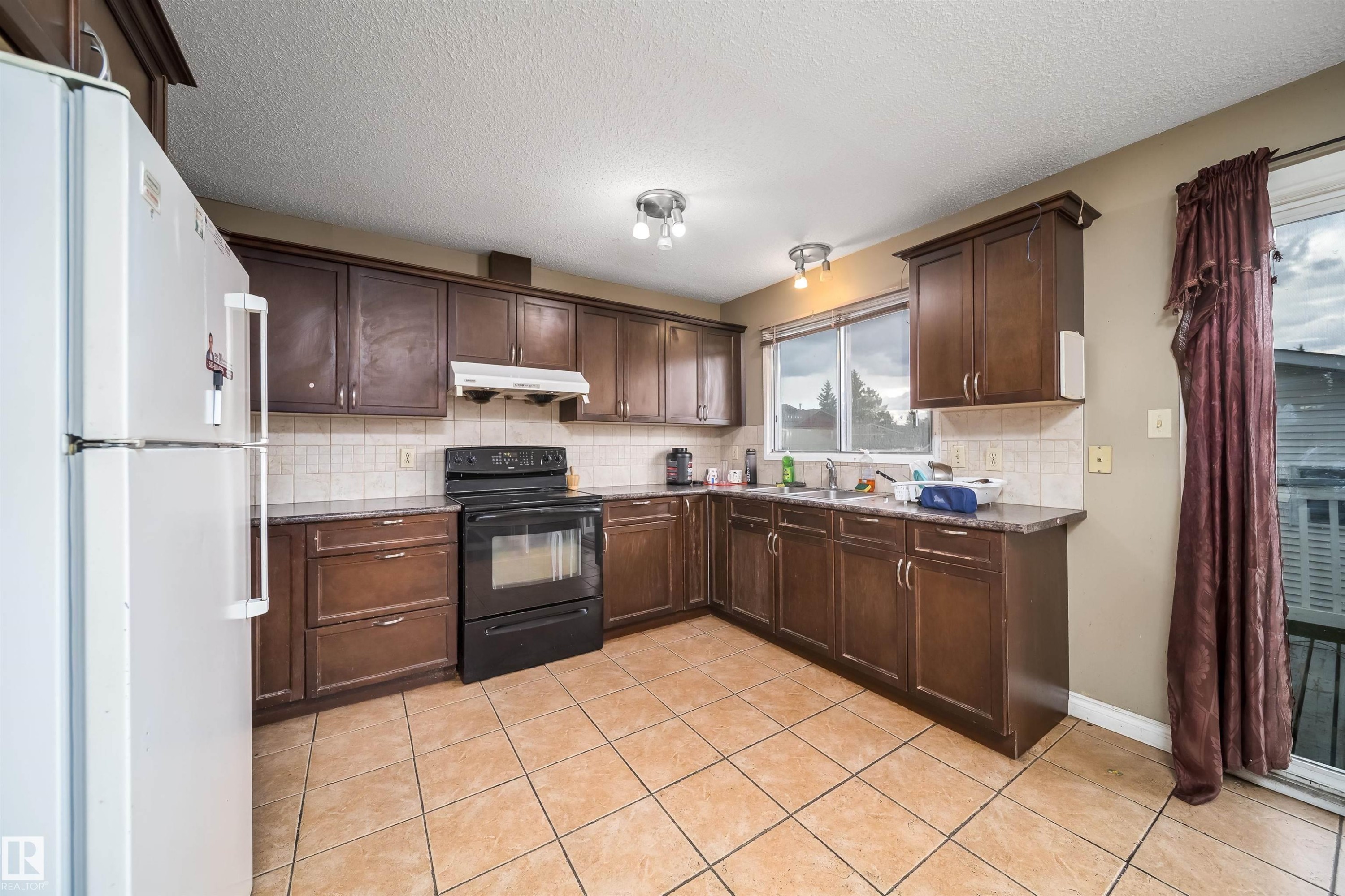 Kitchen featuring dark wood-finish cabinetry, tile flooring, a built-in range, a white tile backsplash, and a sliding glass door - 1771 37 Street, Edmonton, AB - Indoor Photo Showing Kitchen