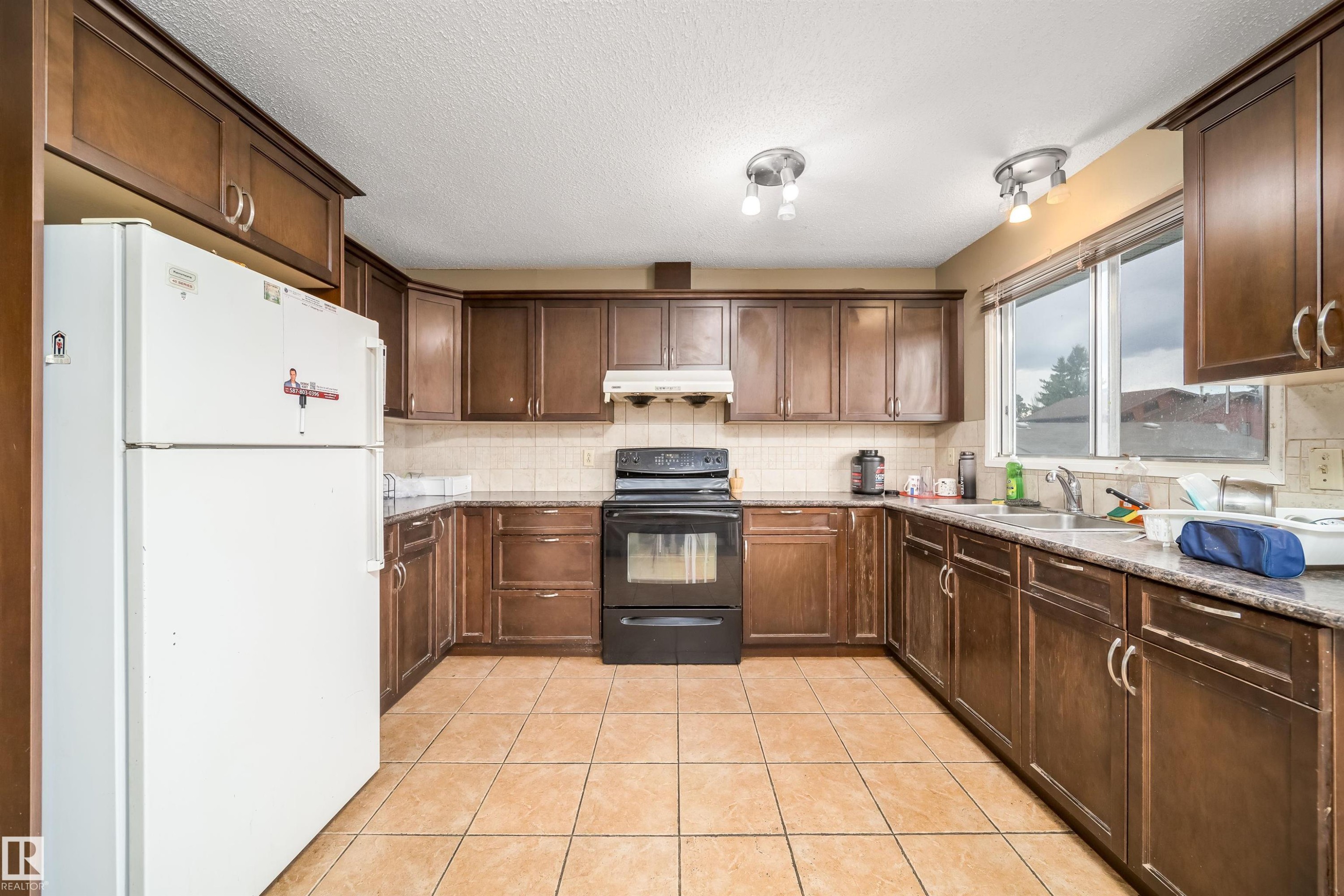 U-shaped kitchen featuring dark wood cabinetry, tile flooring, a window above the sink, a range, and a refrigerator - 1771 37 Street, Edmonton, AB - Indoor Photo Showing Kitchen With Double Sink