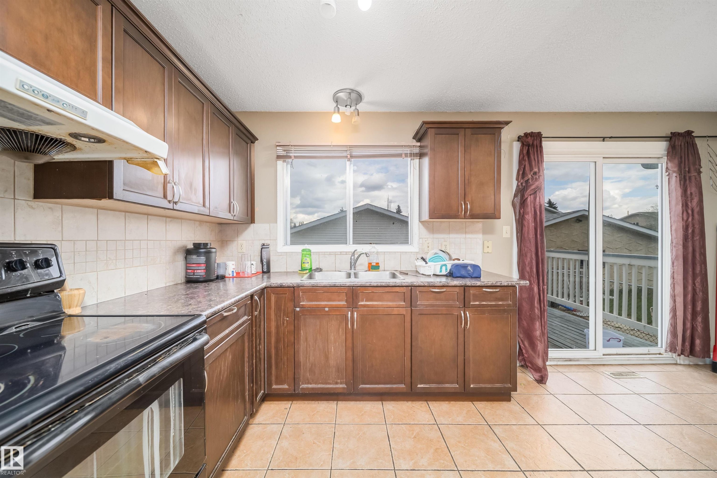 Kitchen featuring wood-finish cabinetry, tile flooring, and a sliding glass door leading to an outdoor deck - 1771 37 Street, Edmonton, AB - Indoor Photo Showing Kitchen With Double Sink