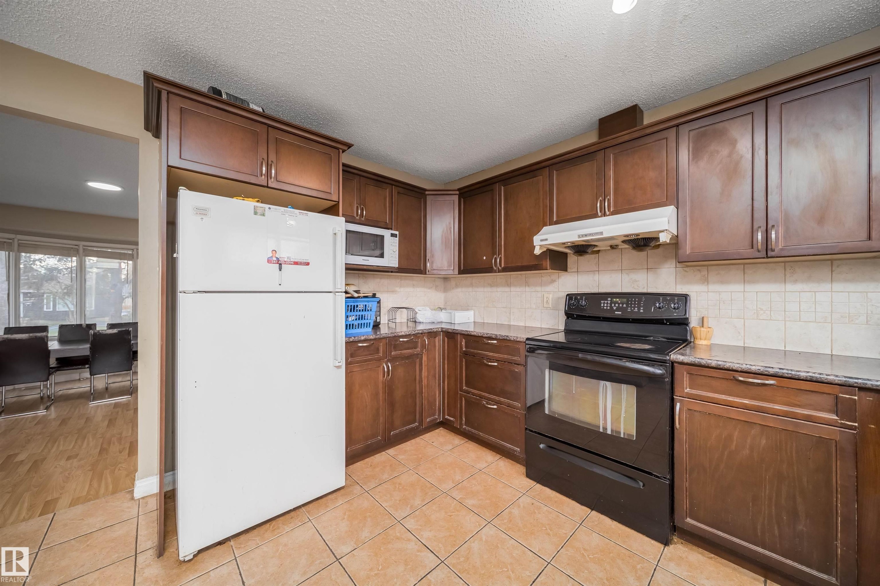 Kitchen featuring tile flooring, wood-finish cabinetry, a black electric range, a white over-the-range microwave, and a tile backsplash - 1771 37 Street, Edmonton, AB - Indoor Photo Showing Kitchen