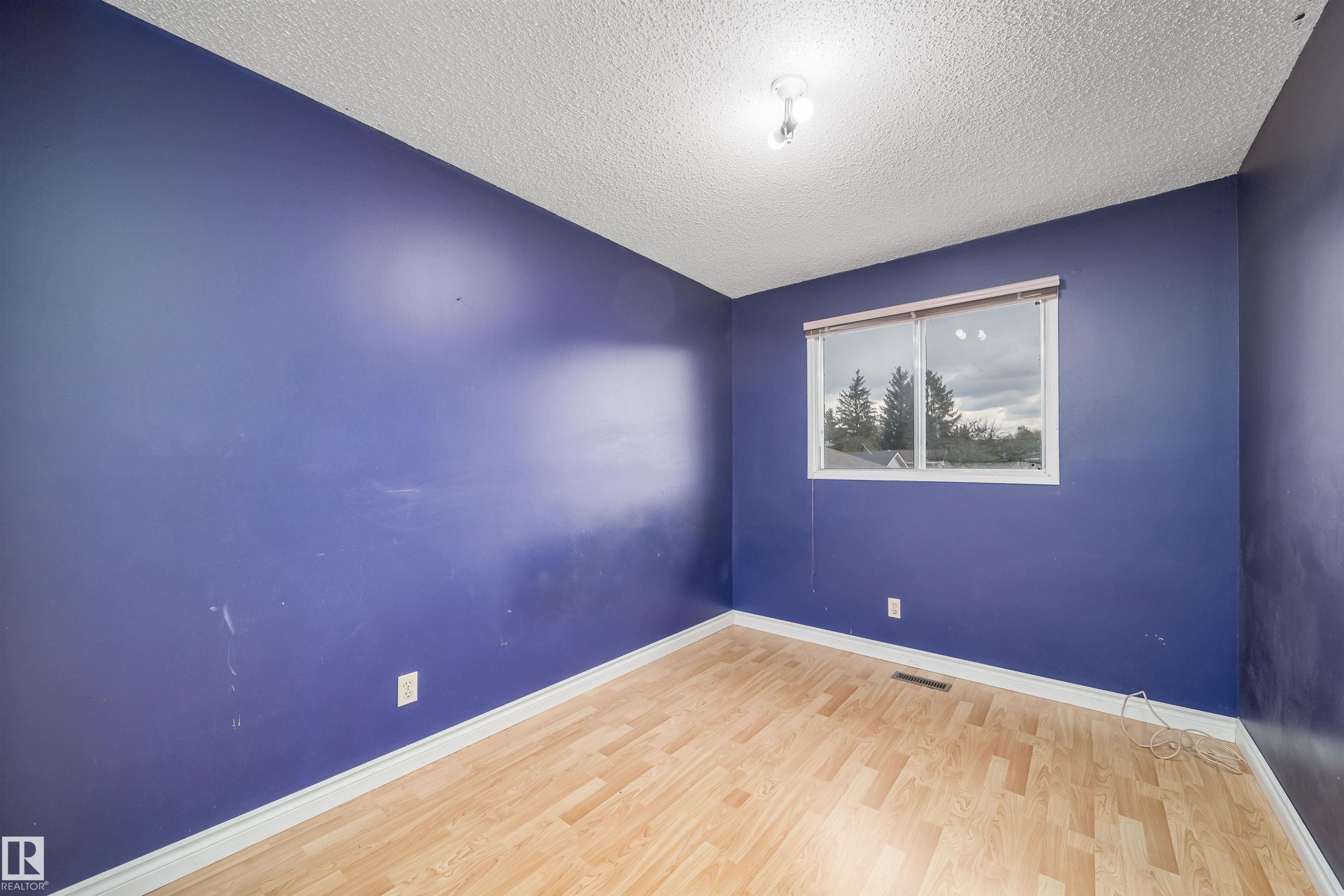 Room featuring wood-finish flooring, a window with a treed backdrop, white baseboards, and a ceiling light fixture - 1771 37 Street, Edmonton, AB - Indoor Photo Showing Other Room