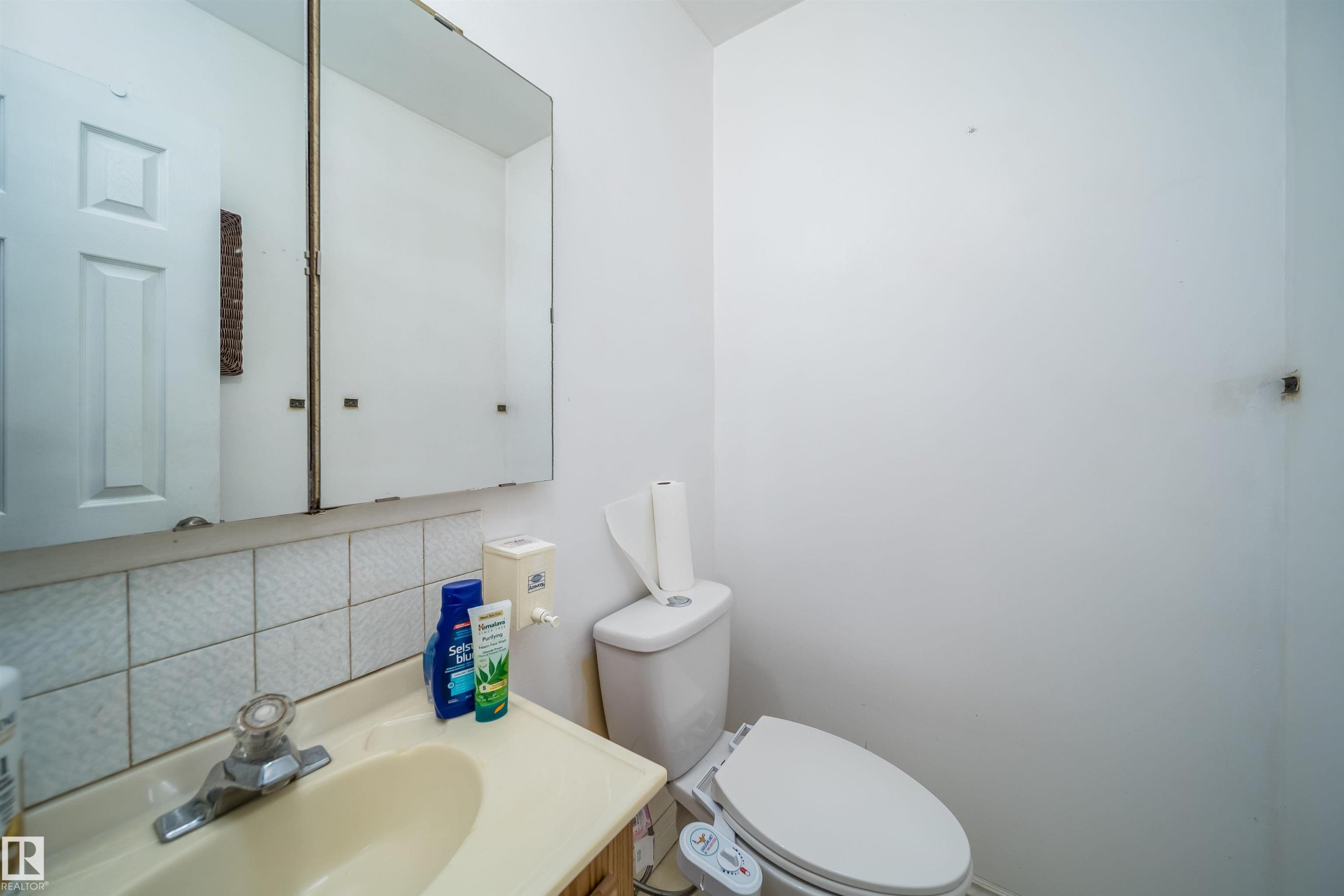 Bathroom featuring a white toilet, wall-mounted medicine cabinet, and a single-handle faucet over a drop-in sink with a tiled backsplash - 1771 37 Street, Edmonton, AB - Indoor Photo Showing Bathroom